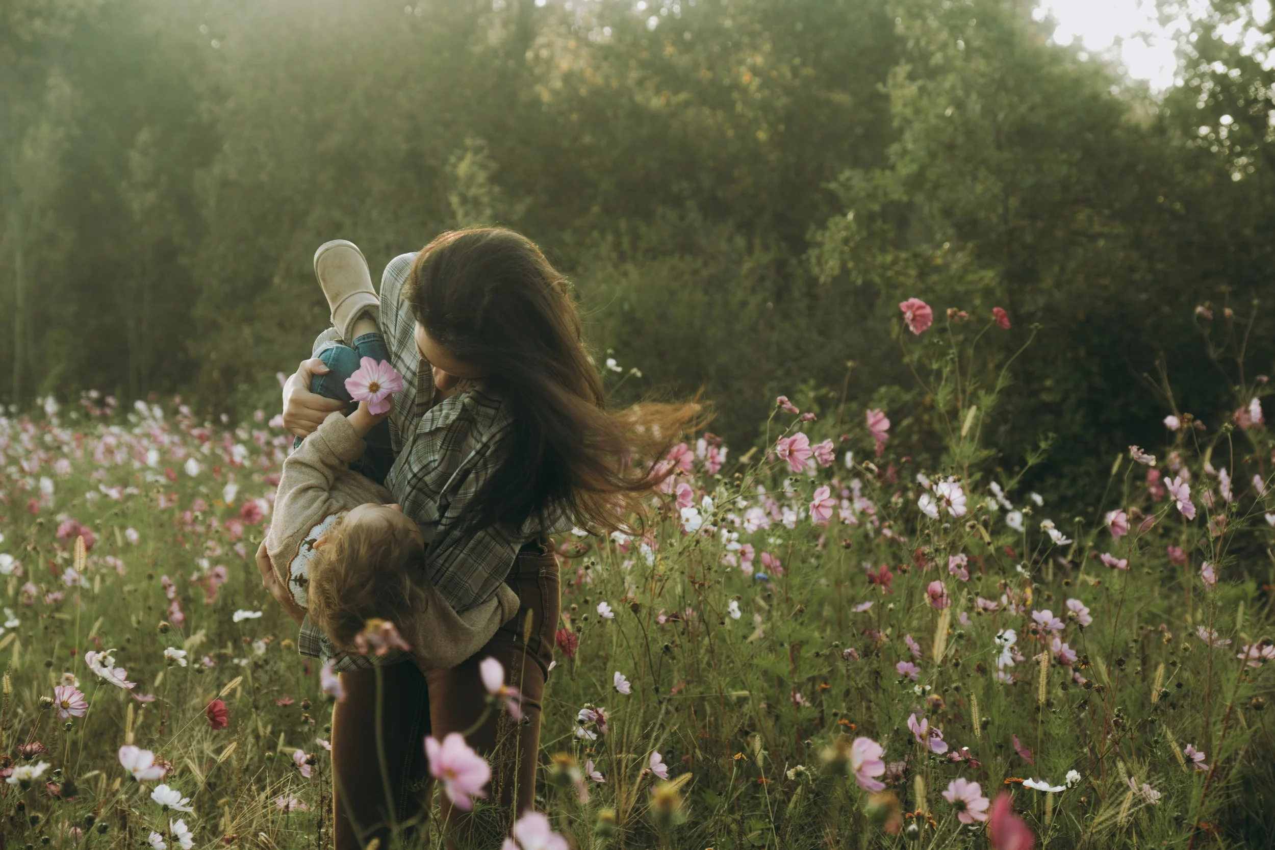 Une femme et un enfant jouent dans un champ de fleurs roses et blanches pendant la journée.