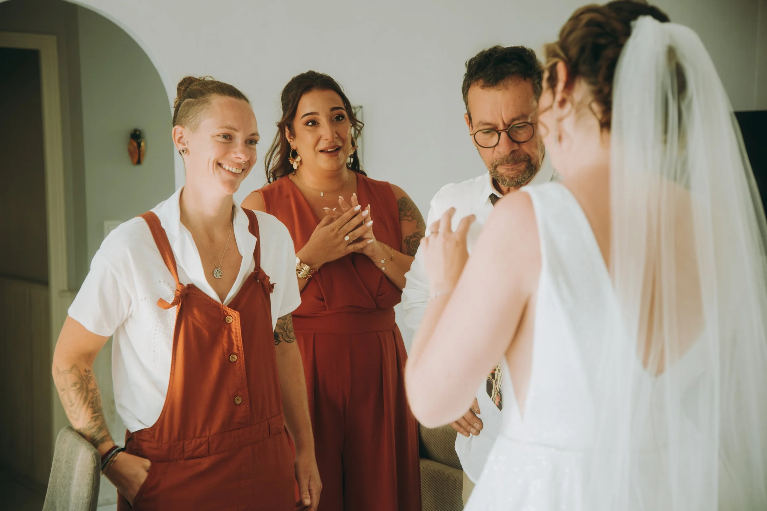 Groupe de personnes lors d'une préparation de mariage, comprenant une femme en robe de mariée et trois autres femmes, dans un intérieur domestique.