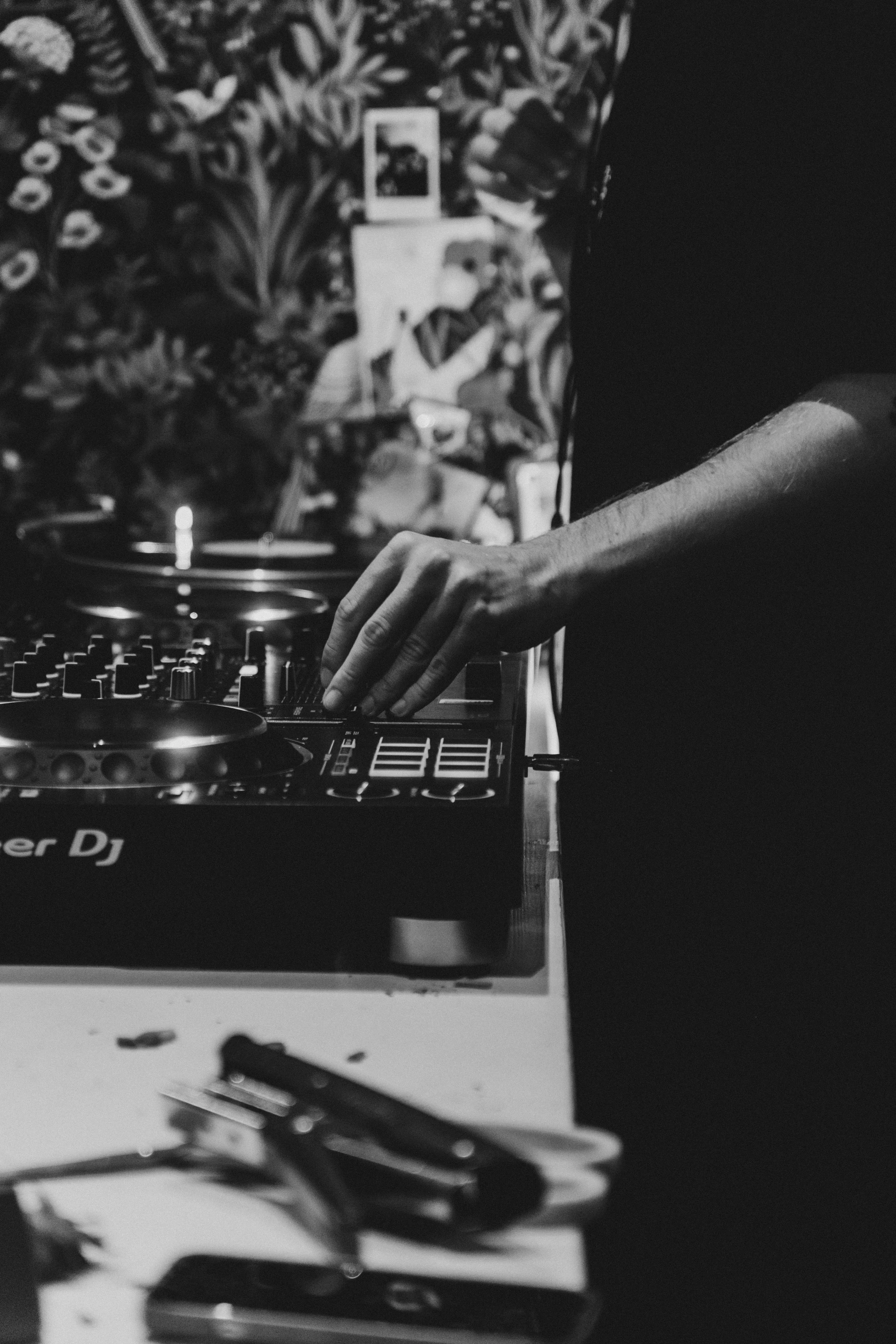 Un DJ manipule un contrôleur de musique dans un environnement sombre, arrière-plan flou avec une personne prenant une photo avec un téléphone.