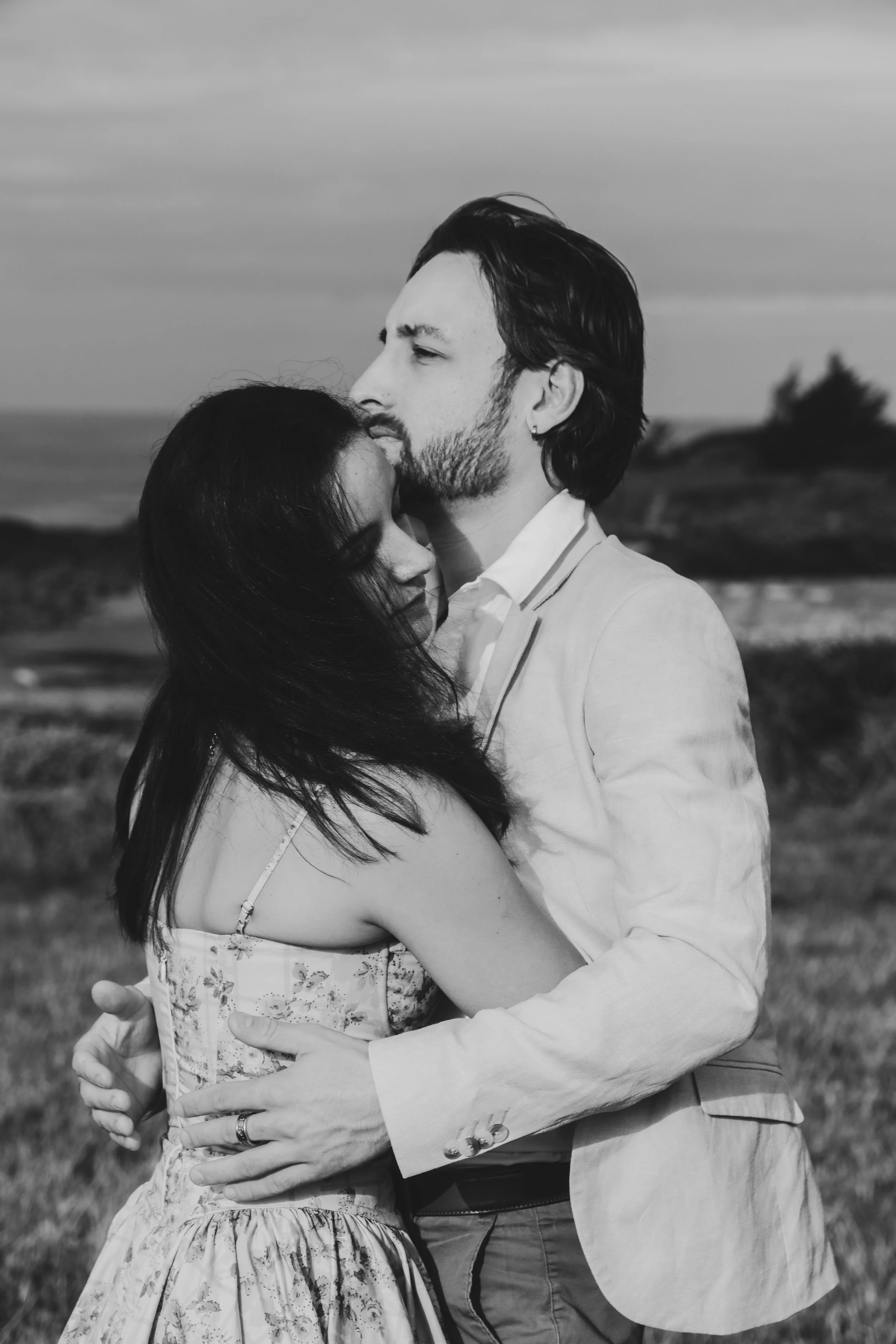 Un couple s'embrasse sur une plage, l'homme a les cheveux longs et une barbe, la femme a les cheveux noirs. La photo est en noir et blanc.