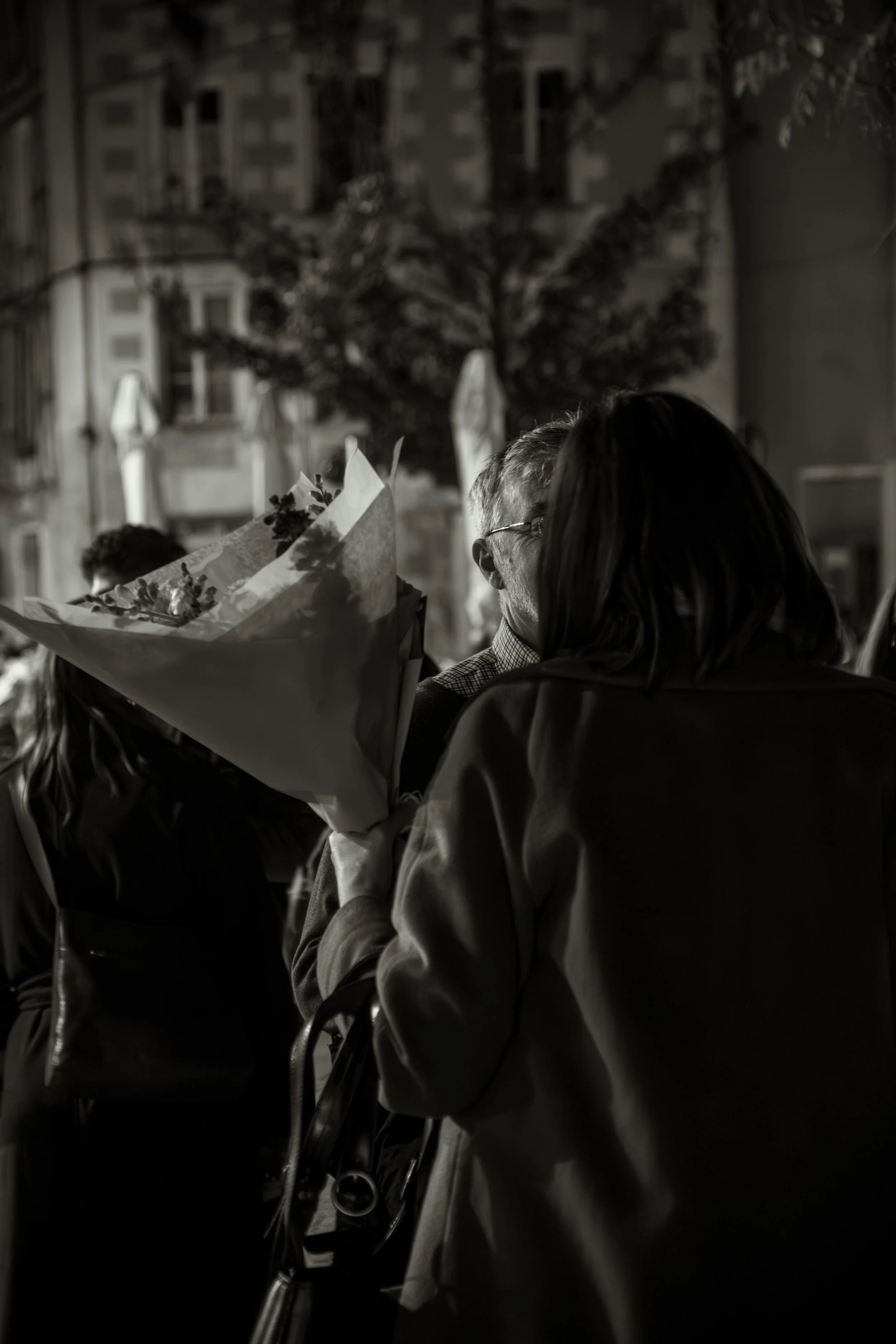 Deux personnes discutent dans une rue la nuit, une d'elles tenant un bouquet de fleurs.