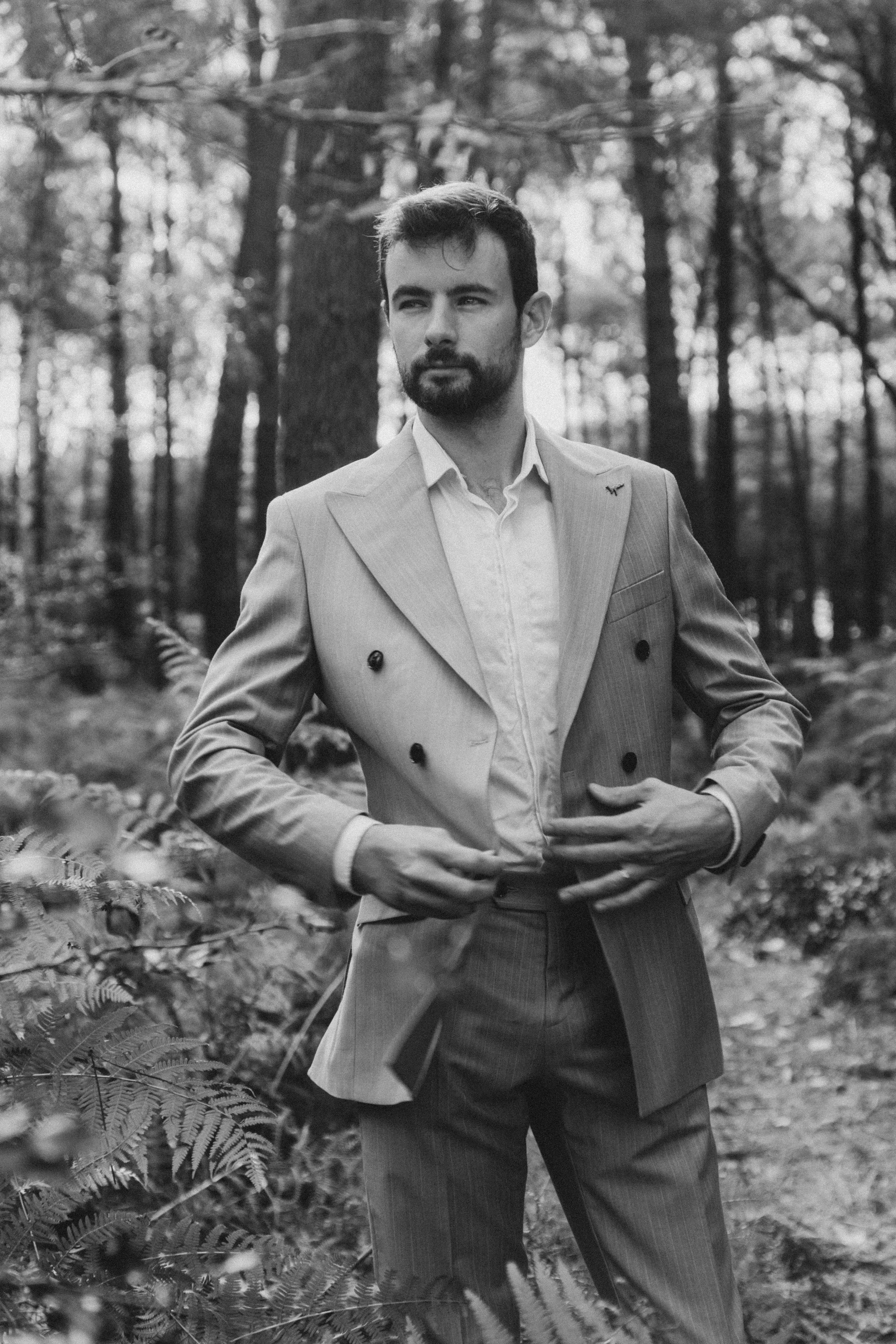 Un homme portant un costume dans une forêt, en noir et blanc.