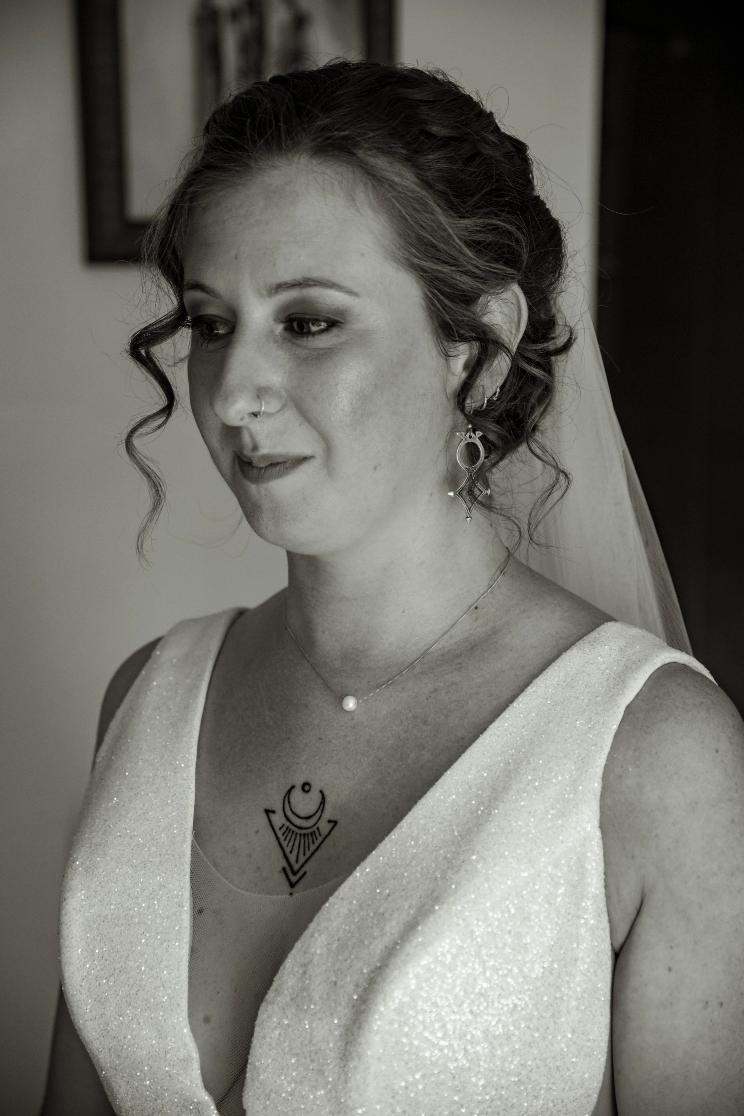 Une femme en robe de mariage avec des boucles d'oreilles et un collier, la tête légèrement inclinée, dans un intérieur