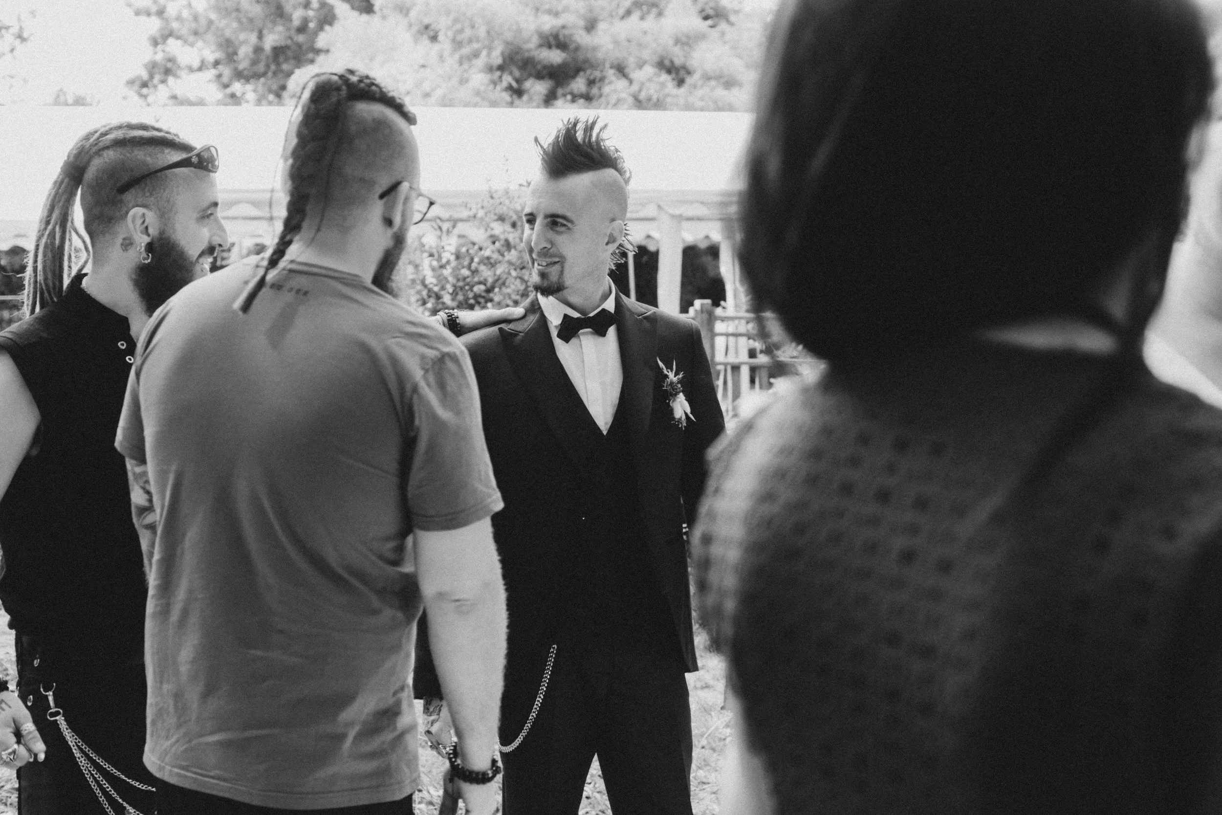 Un groupe de personnes, avec un homme en costume avec un nœud papillon, semble discuter lors d'un événement en plein air.