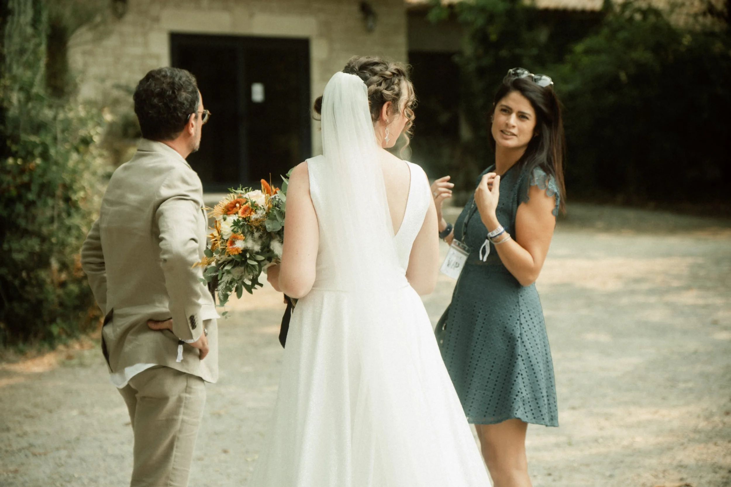 Une femme en robe de mariée parlant avec une femme et un homme lors d'une rencontre en extérieur.