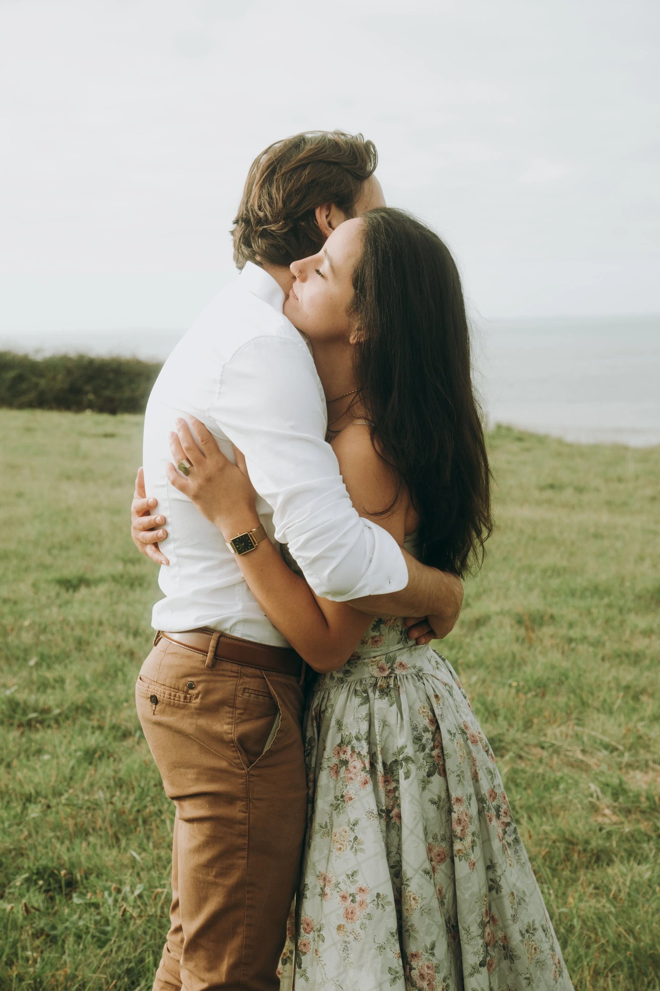 Un couple s'embrasse dans un champ près de la mer par une journée nuageuse.
