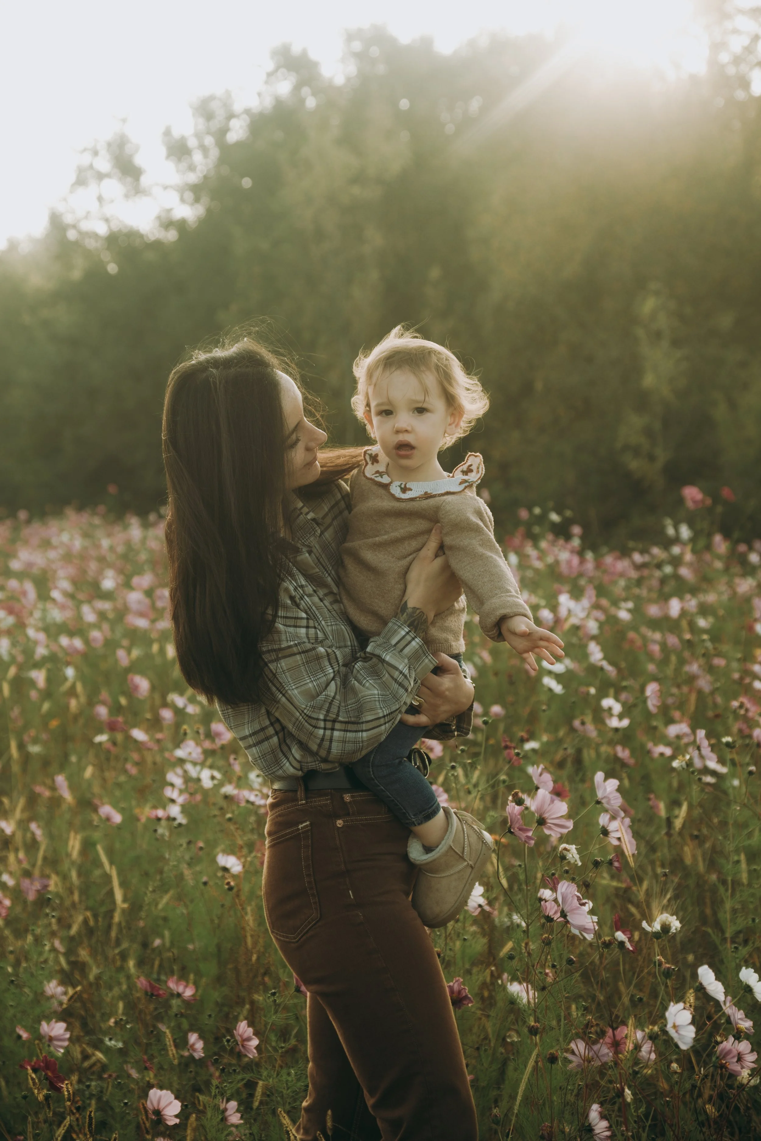 Une femme tenant un enfant dans un champ de fleurs au coucher du soleil.