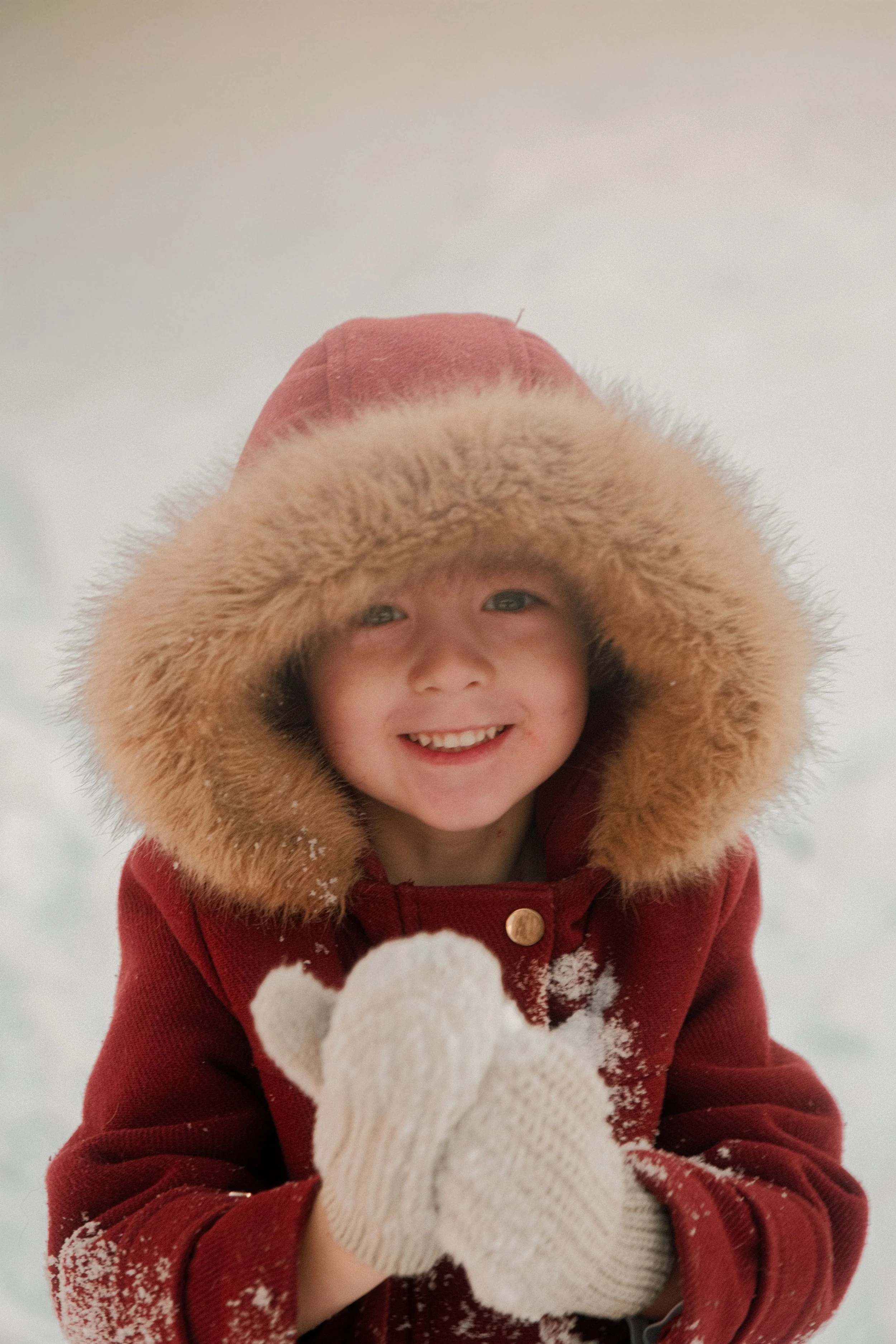 Jeune enfant souriant, hiver, vêtement chaud avec capuche en fourrure, en train de jouer dans la neige.