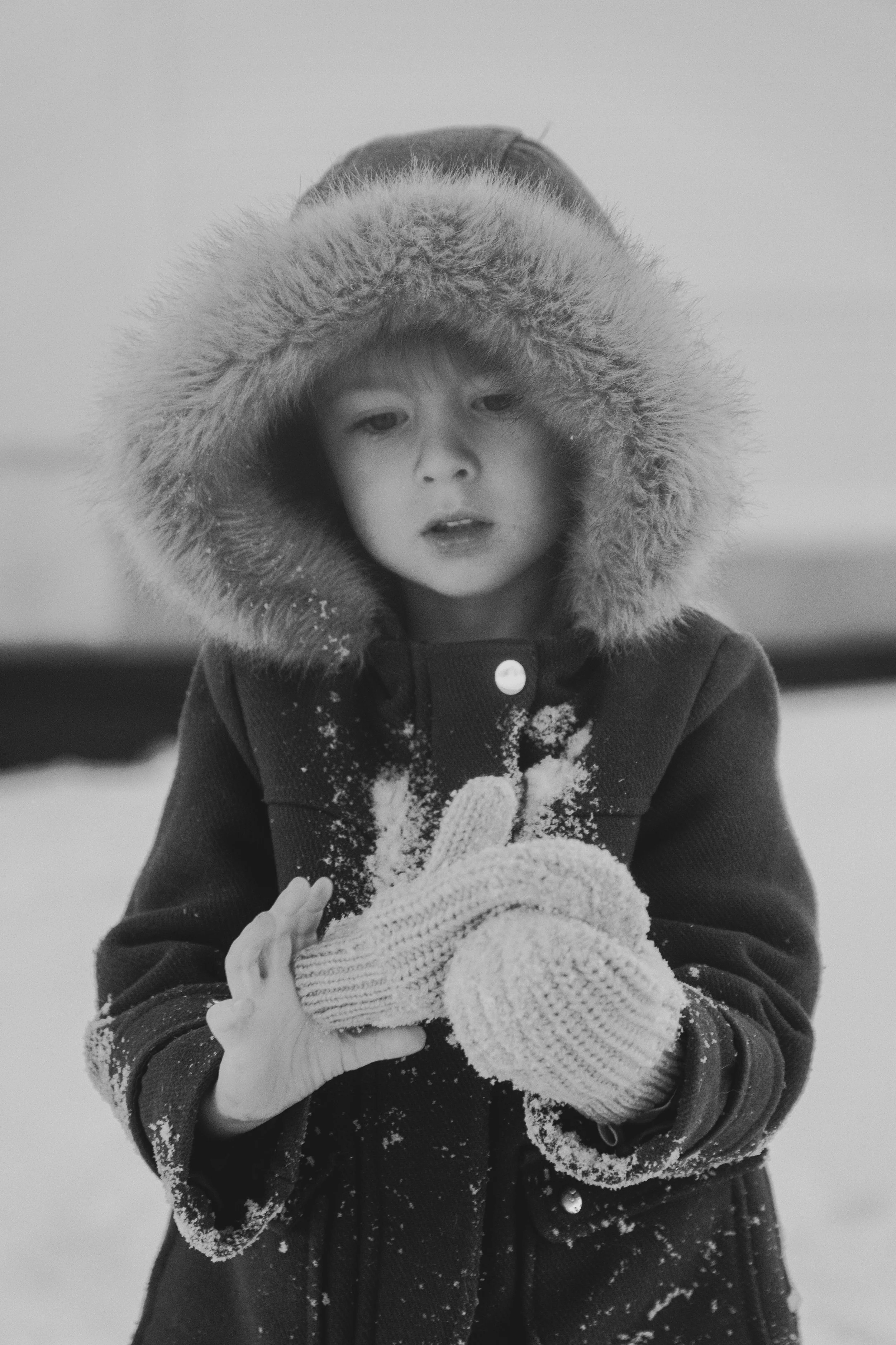 Jeune enfant en manteau à capuche en fourrure, portant des gants en laine, dans la neige.