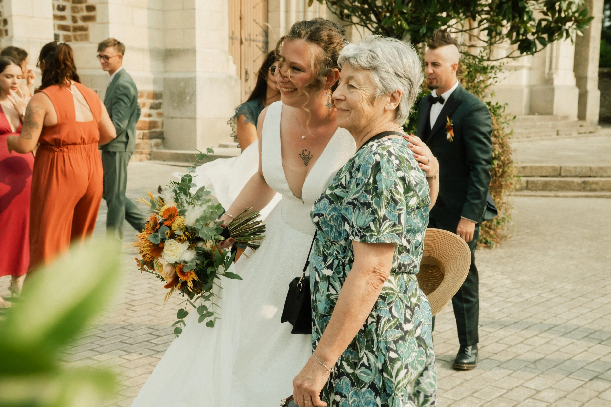 Une mariée en robe blanche joyeuse en compagnie d'une femme âgée lors d'un mariage en plein air.