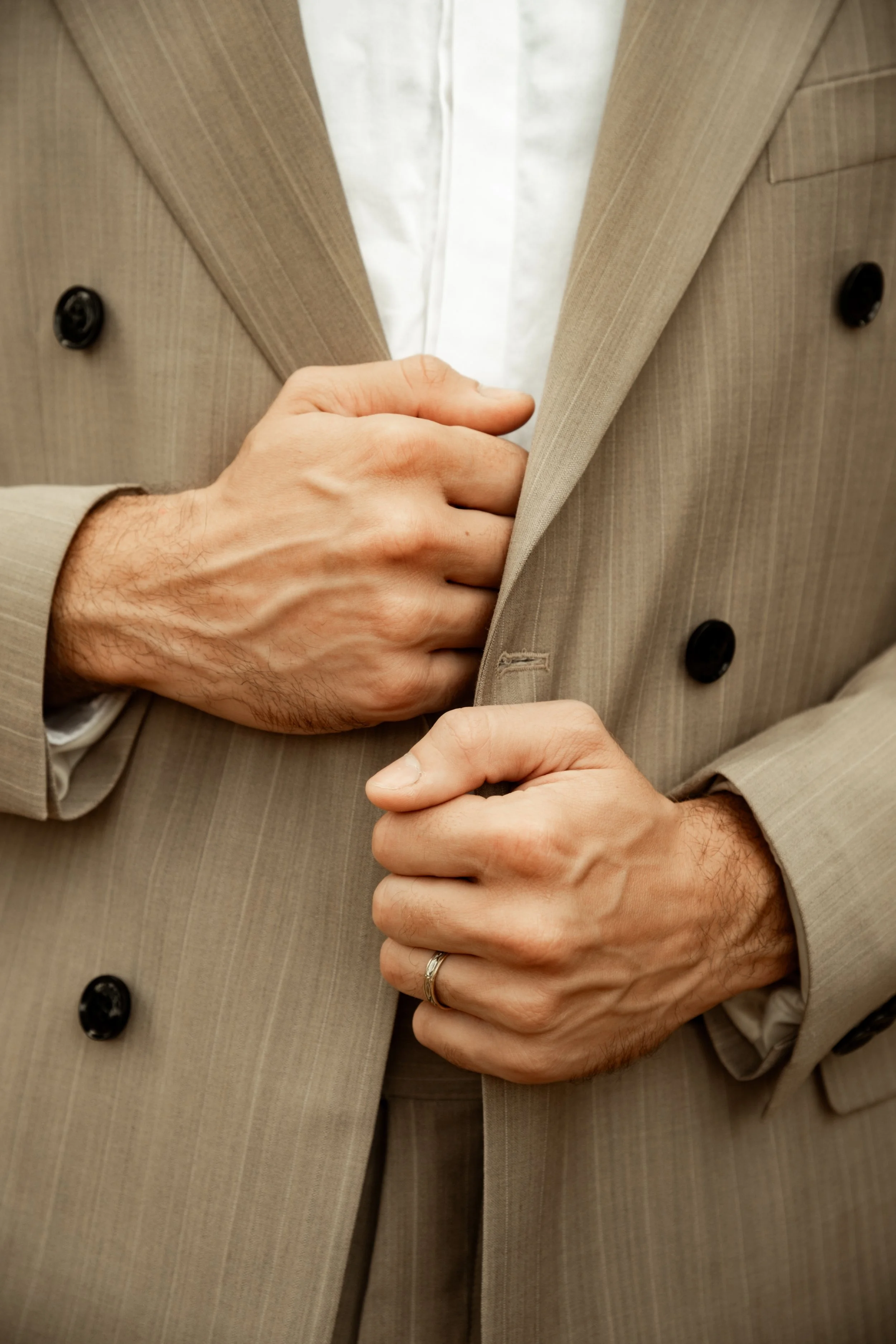 Image d'une personne ajustant ou fermant le bouton de sa veste beige. La personne porte une alliance à la main gauche.
