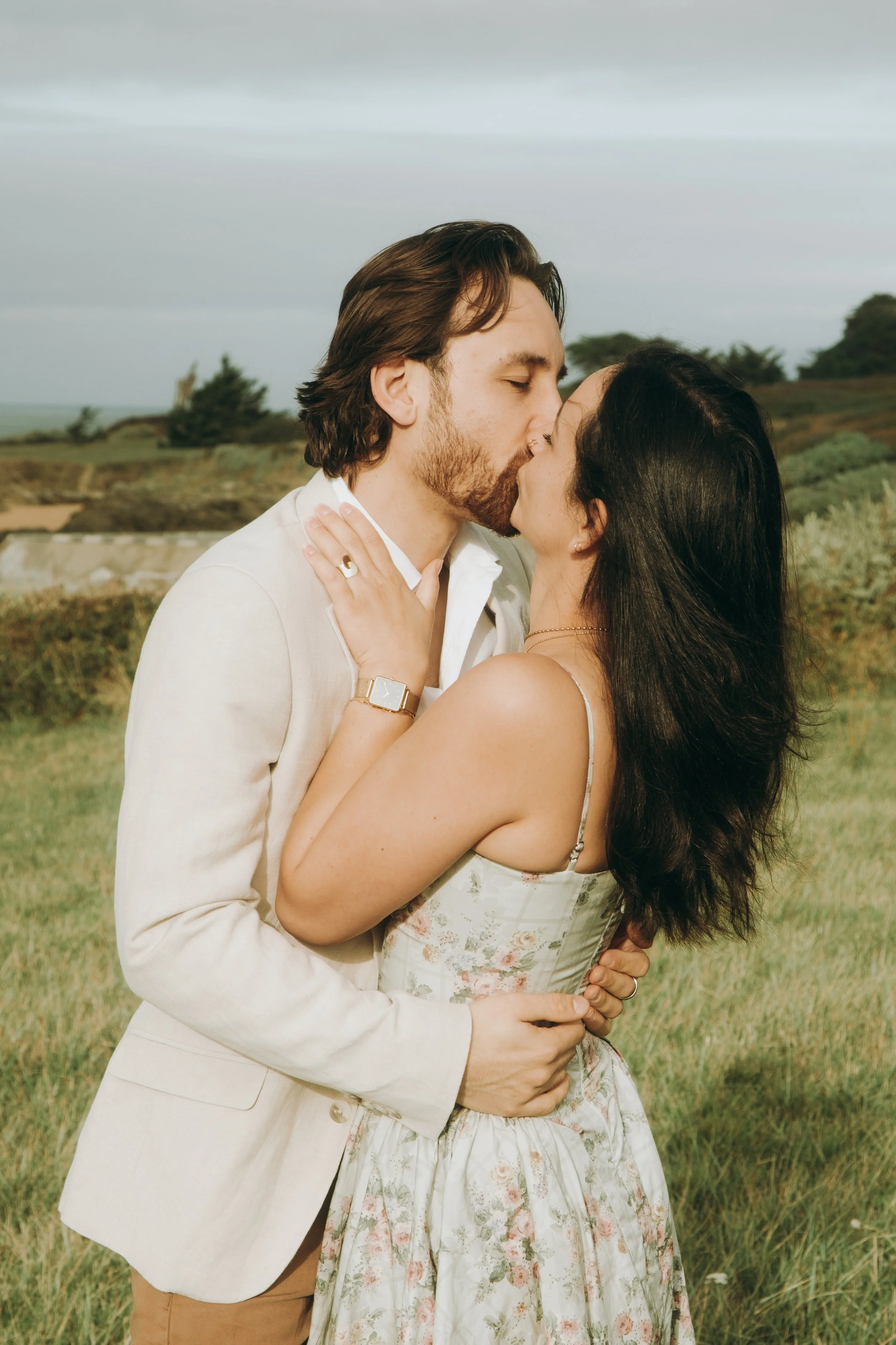 Un couple en maillot de bain blanc s'embrasse dans un champ vert avec un ciel nuageux.