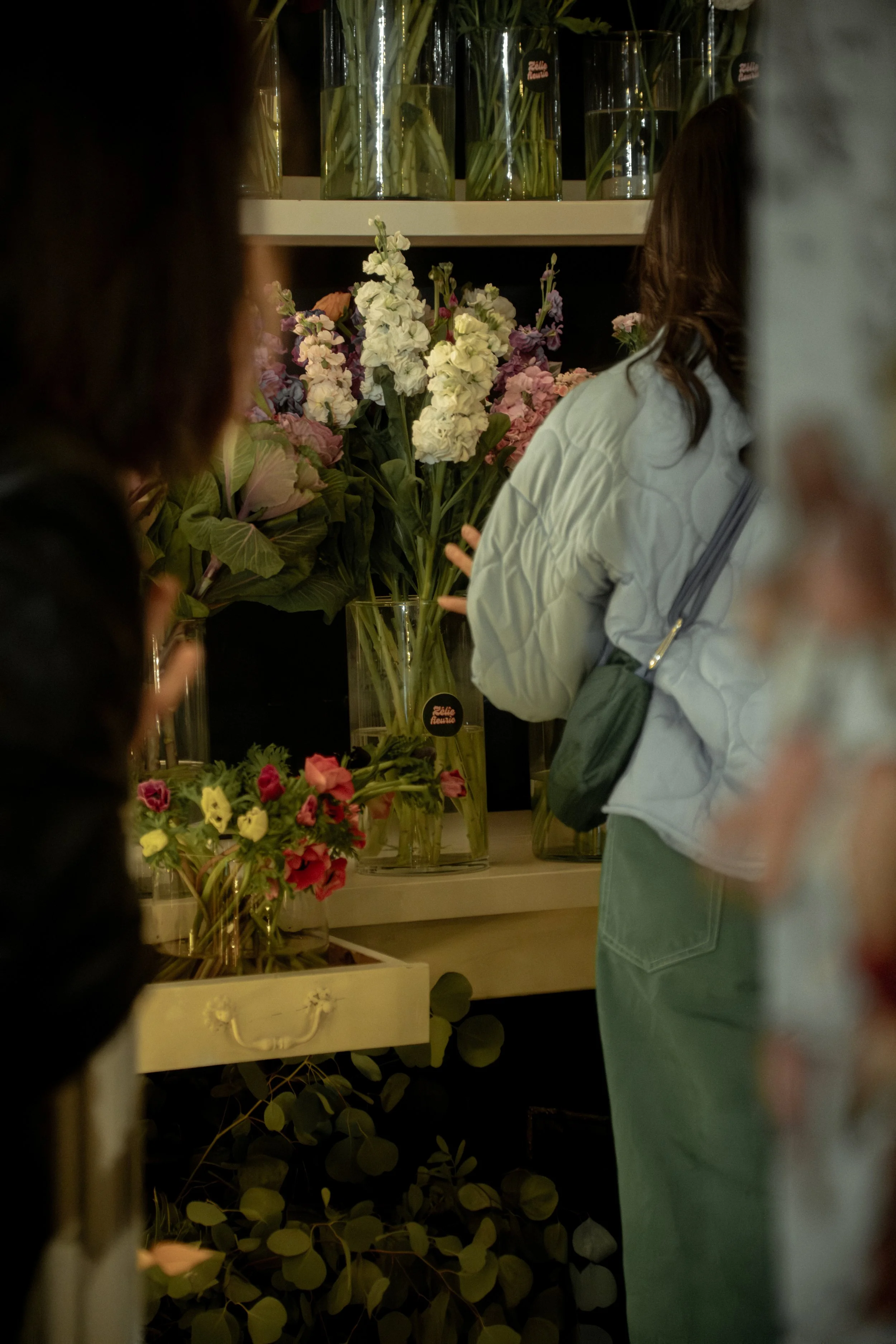 Personne achetant ou regardant des fleurs dans une boutique, avec des vases de fleurs colorées sur une étagère en arrière-plan.