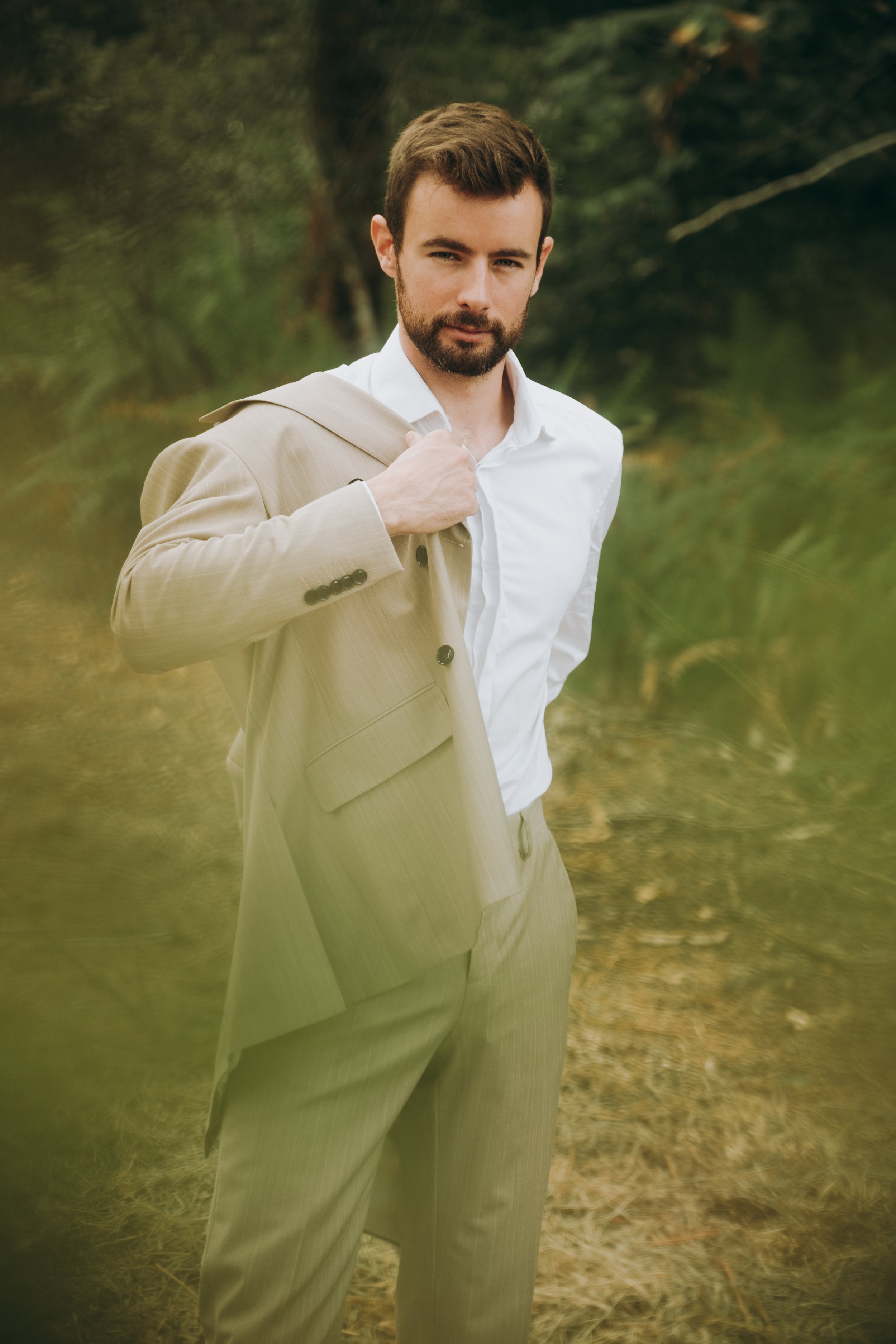 Un homme portant un costume beige et une chemise blanche dans une forêt.