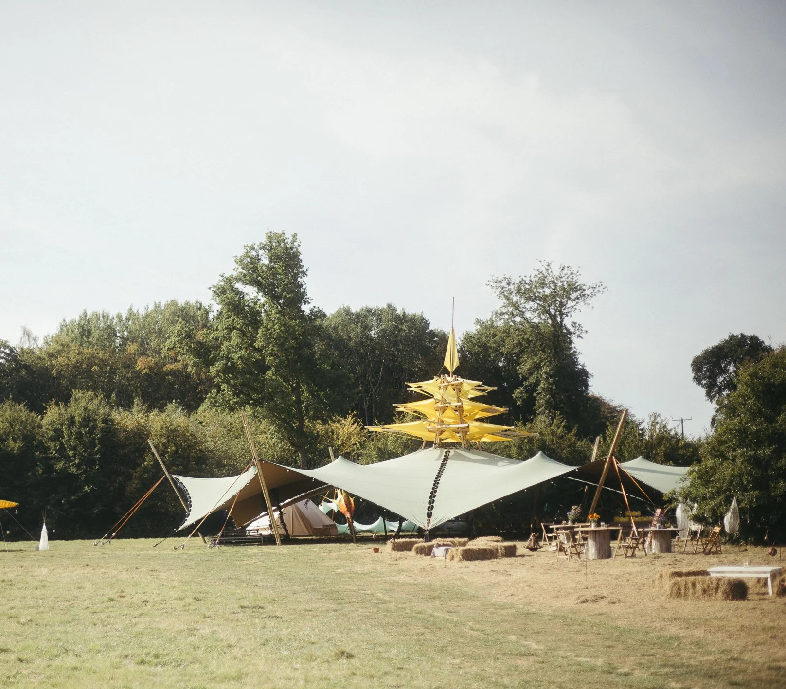 A large outdoor event tent with a yellow spire, set up on a grassy field surrounded by trees.