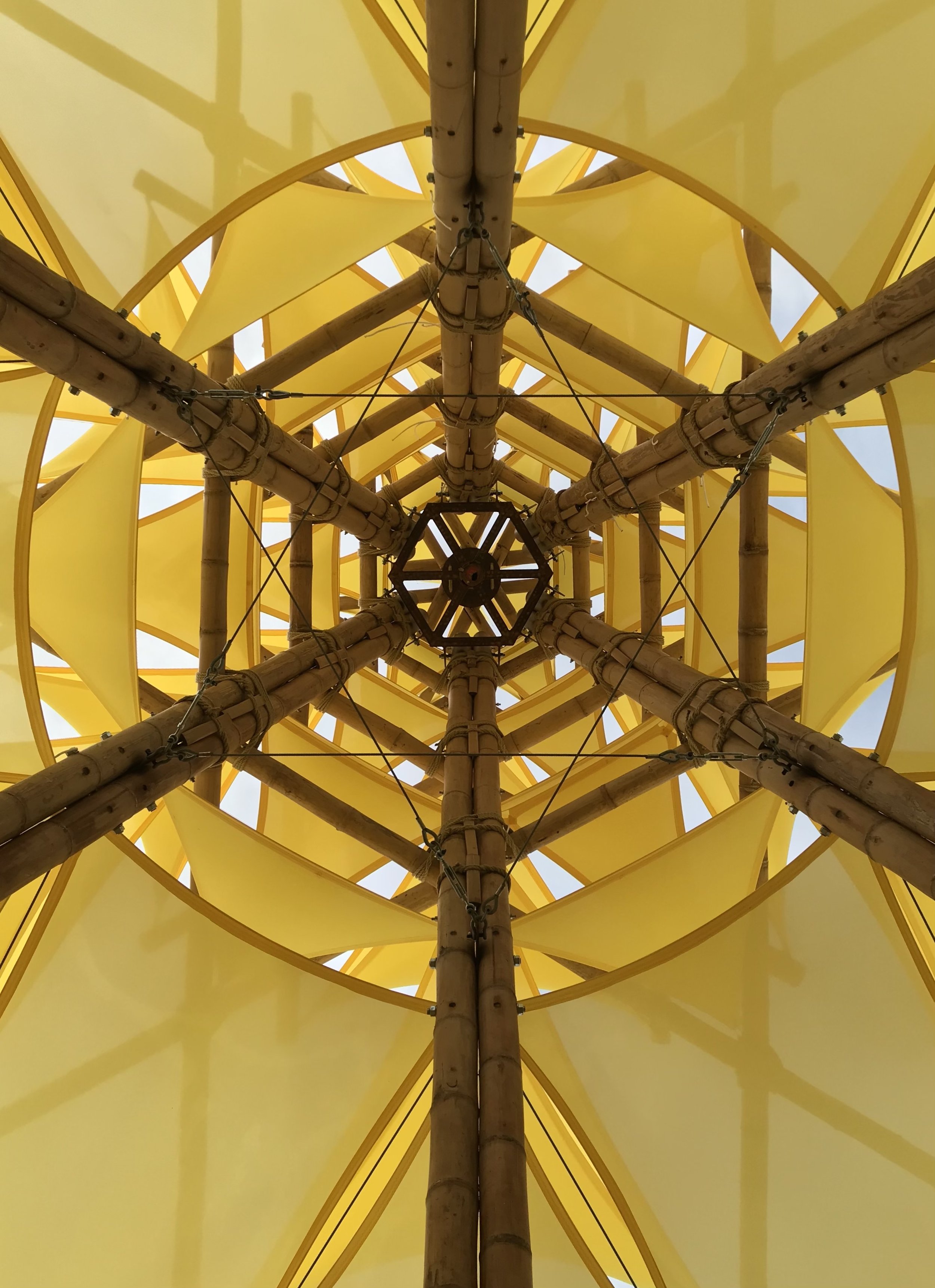 Looking up at the bottom of a yellow spiral-shaped structure with bamboo poles and metal brackets.