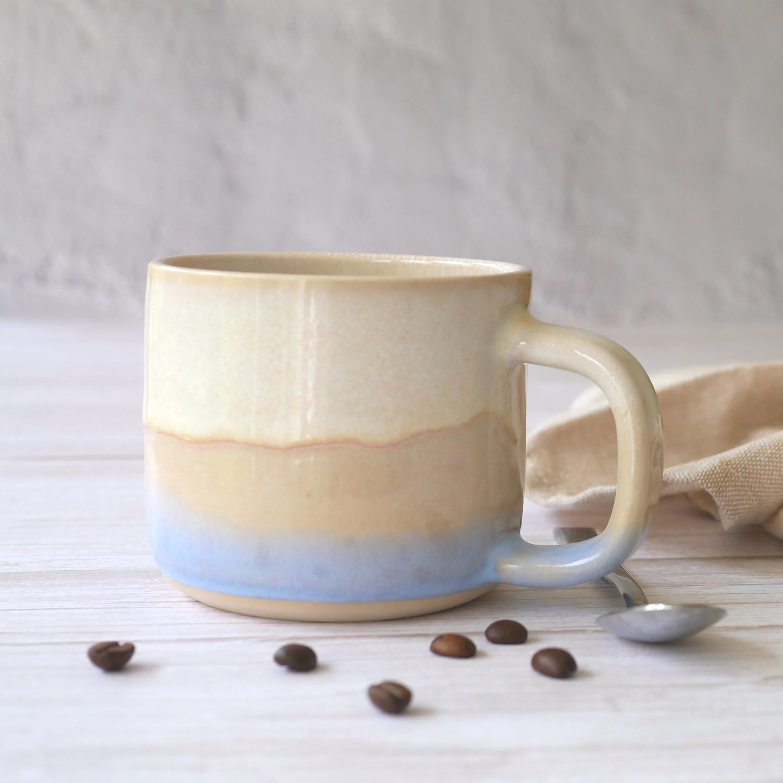 Hand-thrown stoneware mug. This mug features a beautiful blend of beige and light blue glazes, creating organic, flowing patterns that make every piece uniquely yours.