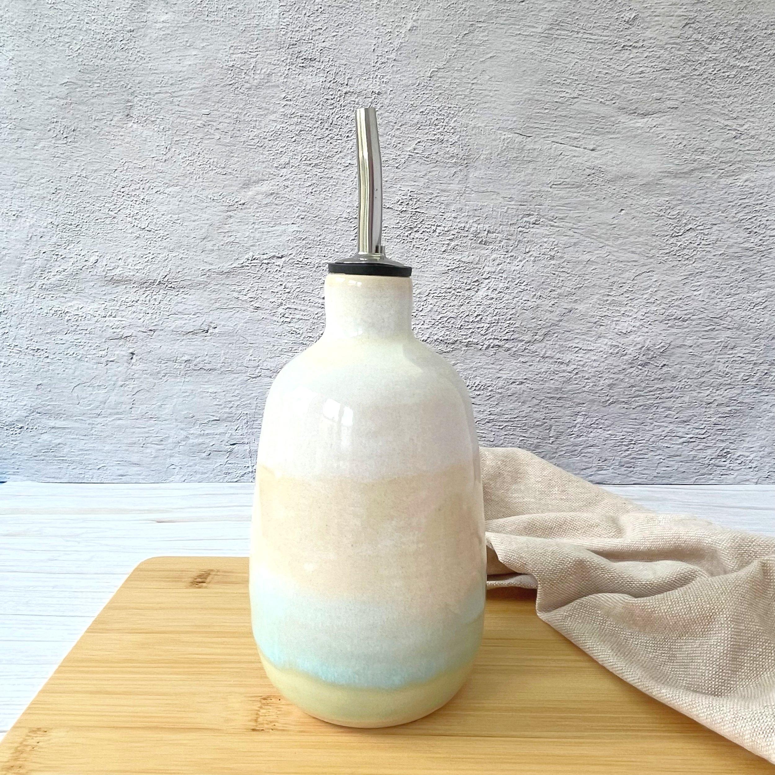 Hand-thrown ceramic oil pourer with turquoise and cream glaze, smooth exterior, and stainless steel spout.