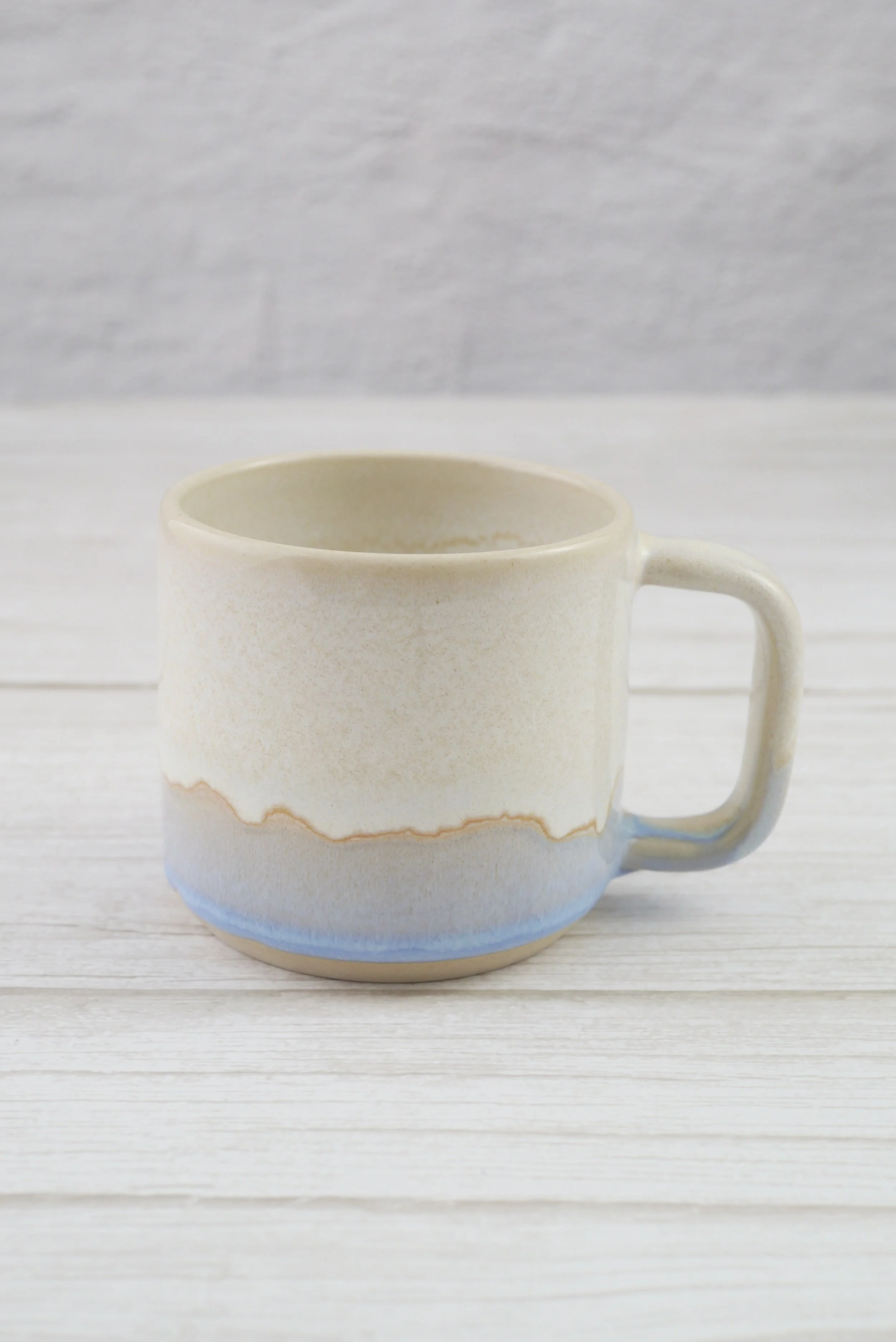 Hand-thrown stoneware mug. This mug features a beautiful blend of beige and light blue glazes, creating organic, flowing patterns that make every piece uniquely yours.
