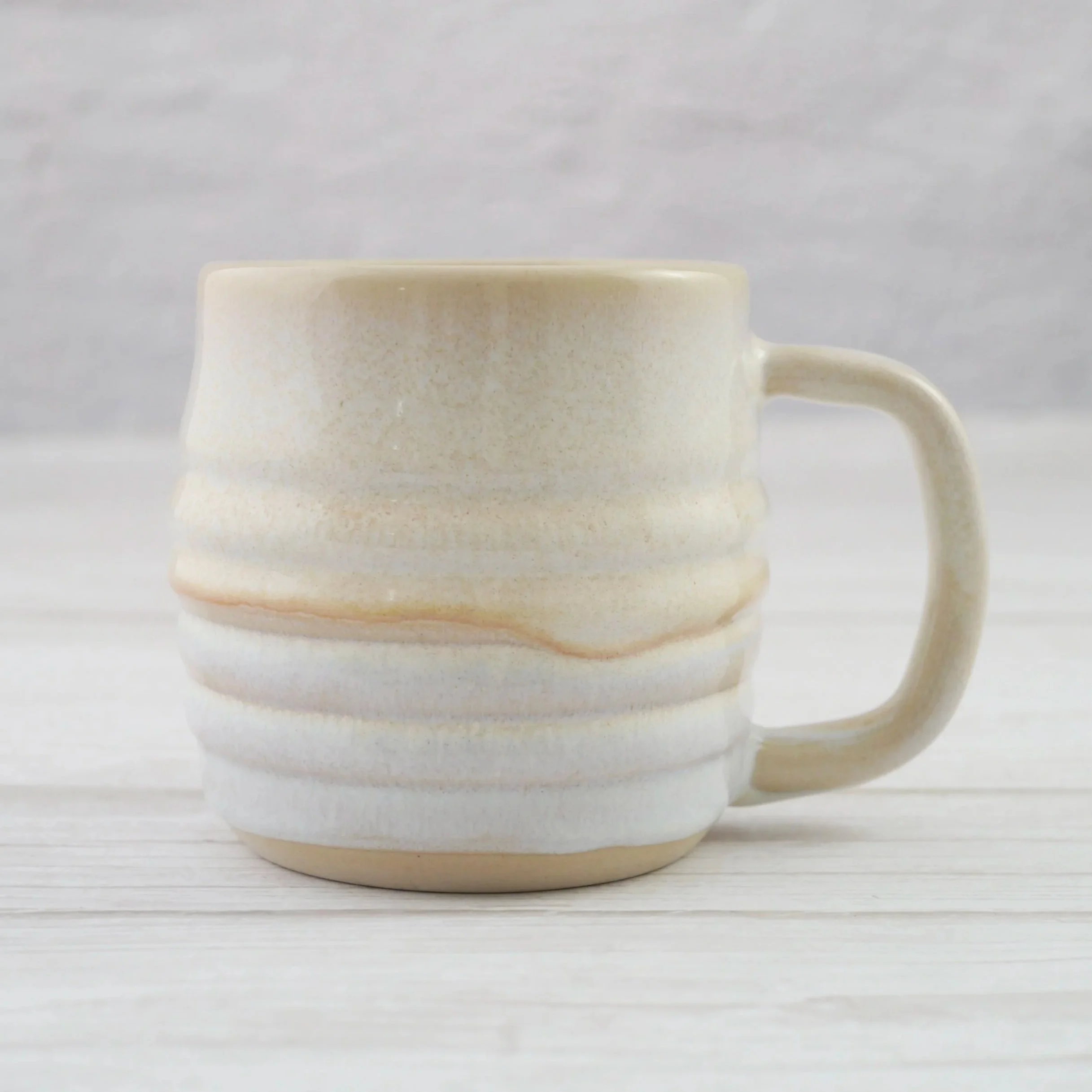 Hand-thrown ceramic mug. This mug features a beautiful blend of beige and white glazes over a rippled exterior, creating organic, flowing patterns that make every piece uniquely yours.
