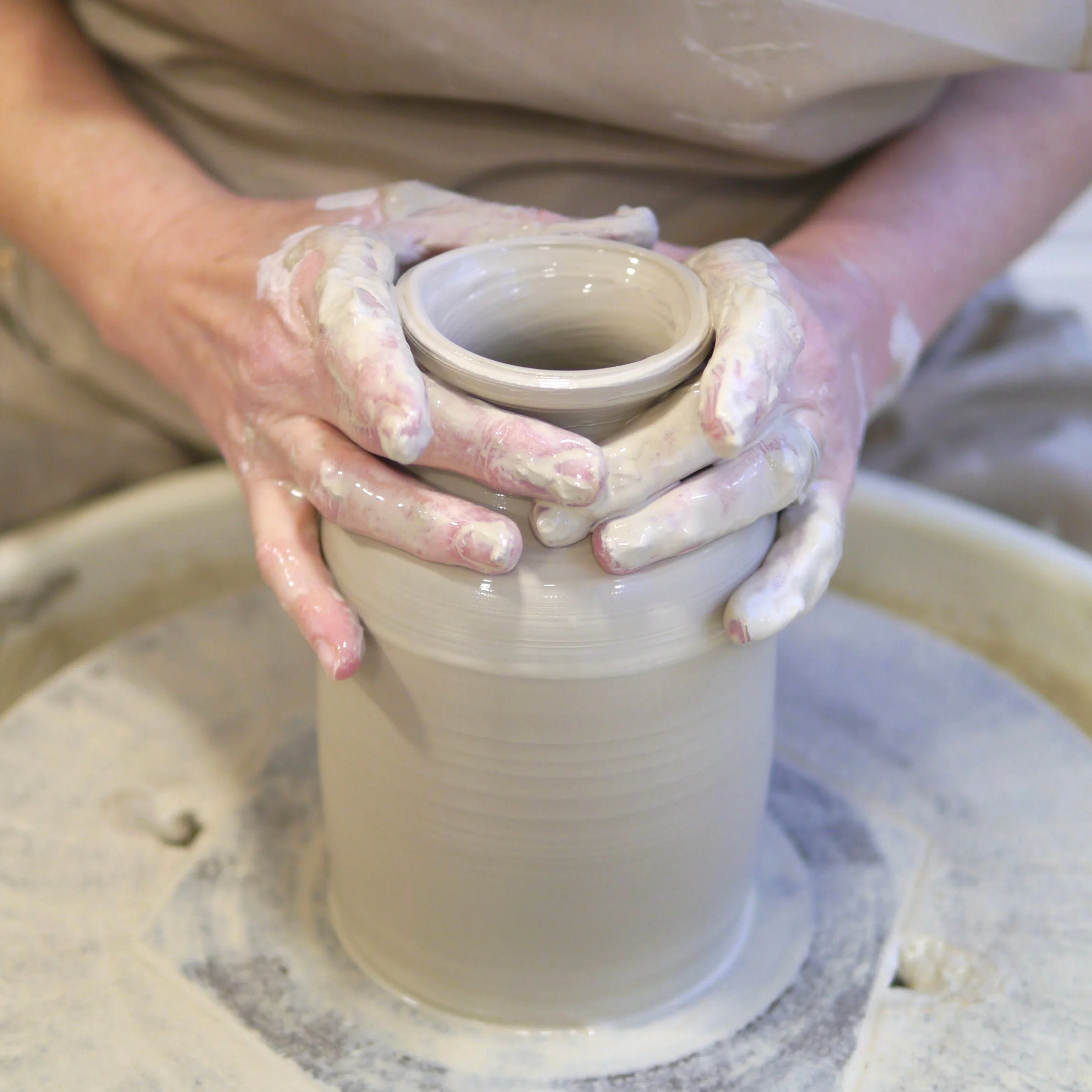 Anna shaping a ceramic vase on her pottery wheel, with her hands covered in wet clay.