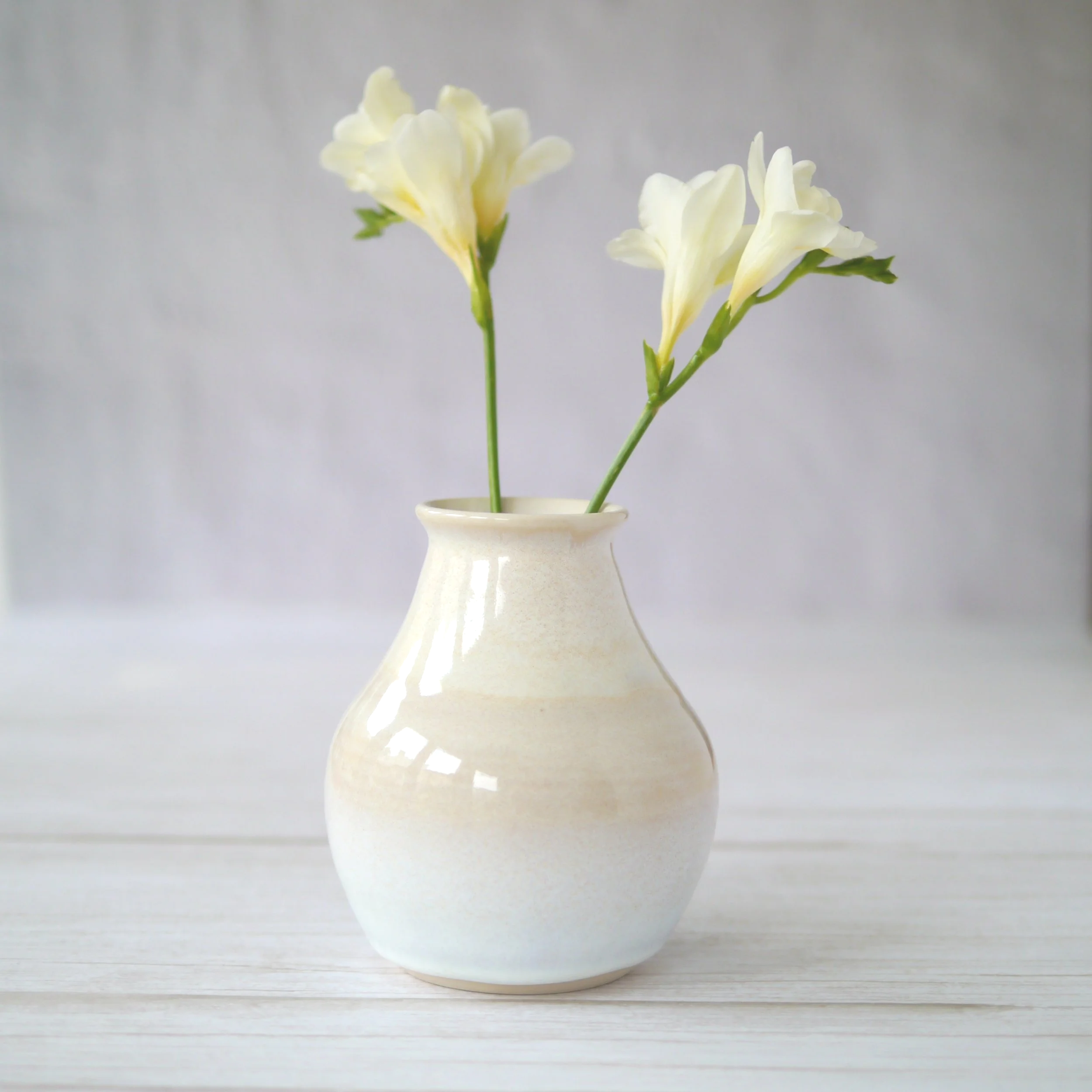 Hand-thrown stoneware vase. The glaze drifts from warm cream through pale oatmeal into soft mist white at the base.