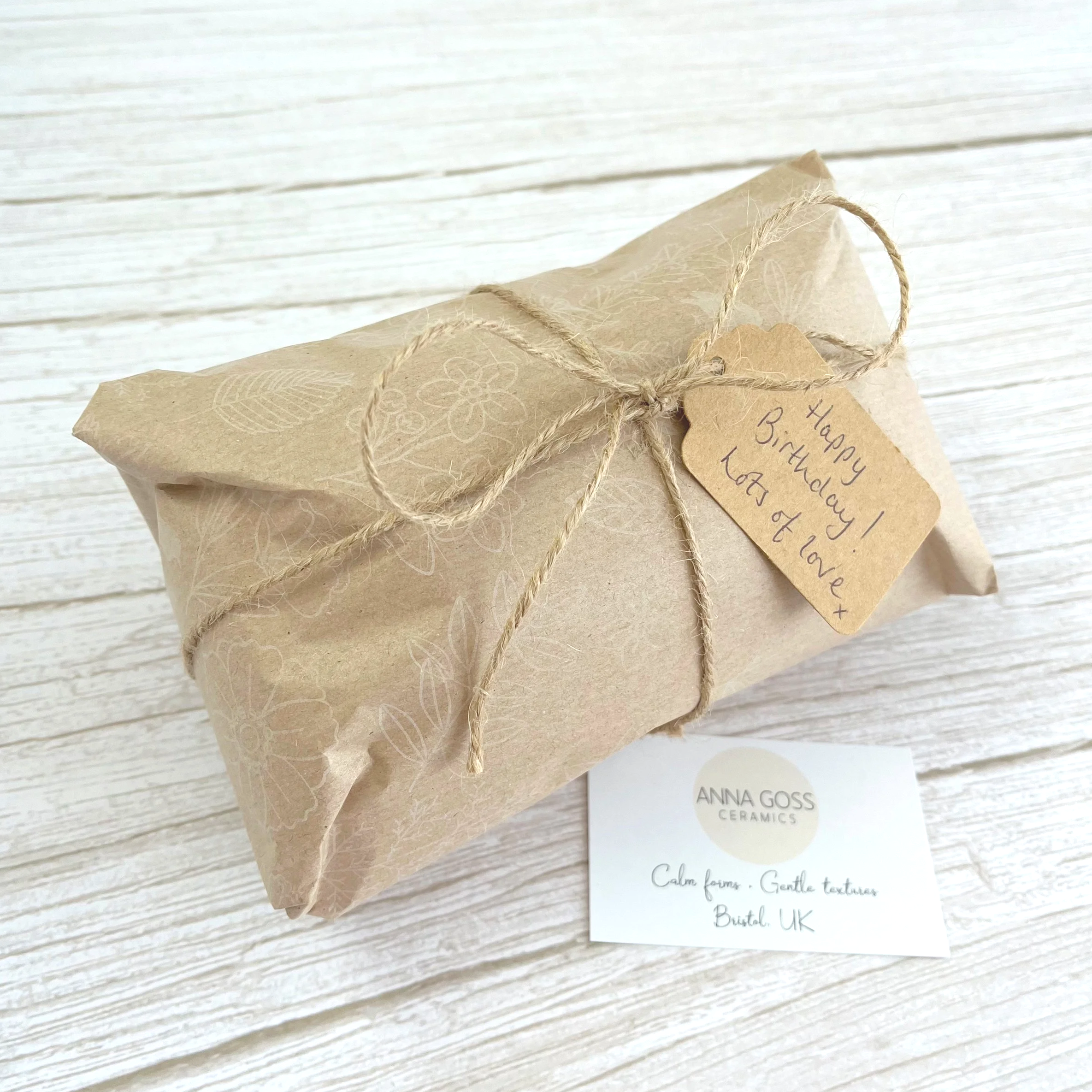 An example of a vase gift wrapped in kraft brown paper with a light white floral design, and finished with natural jute string and a hand-written kraft gift tag.