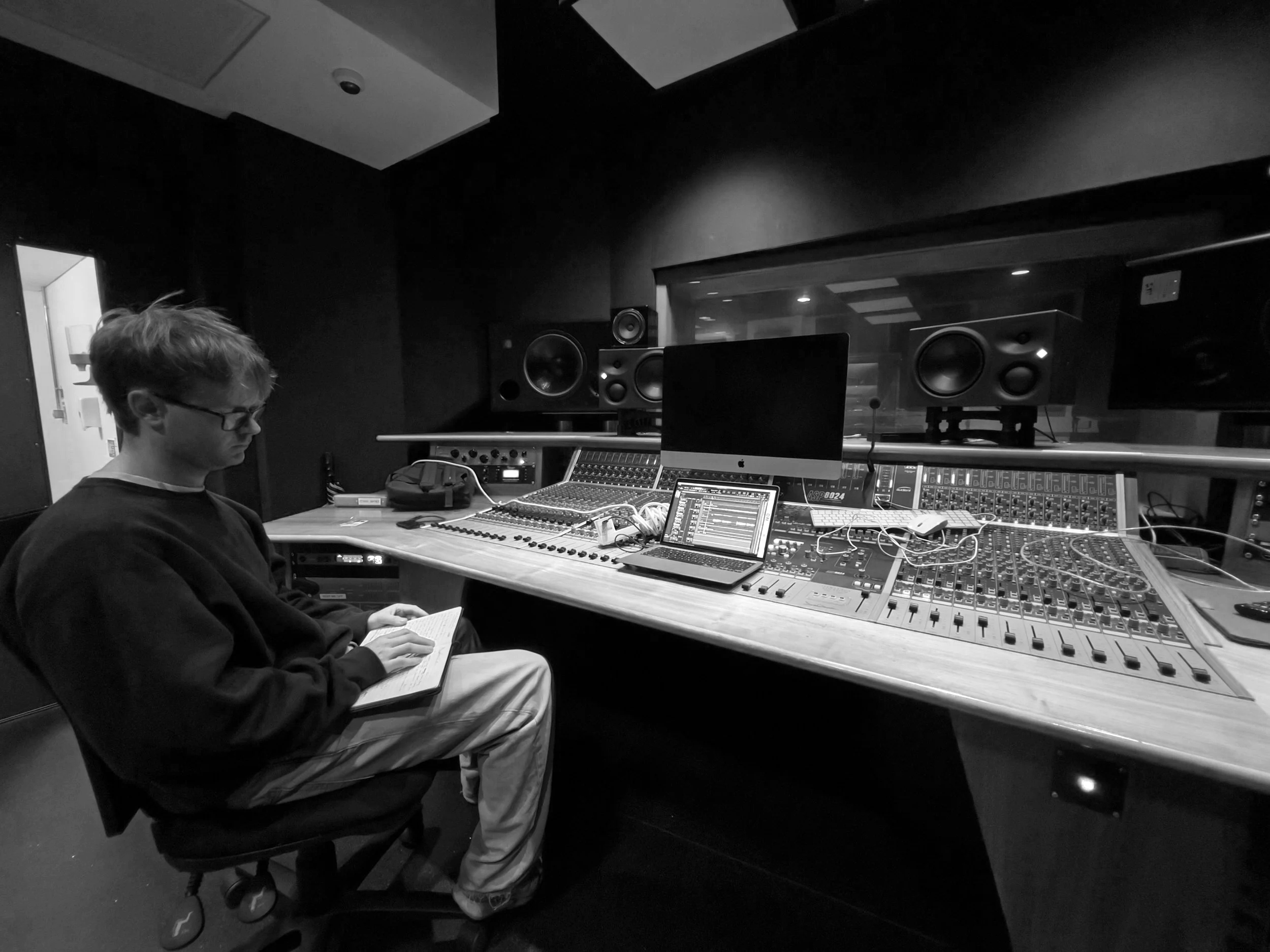 A person sitting in front of audio mixing equipment in a recording studio, reading a notebook.