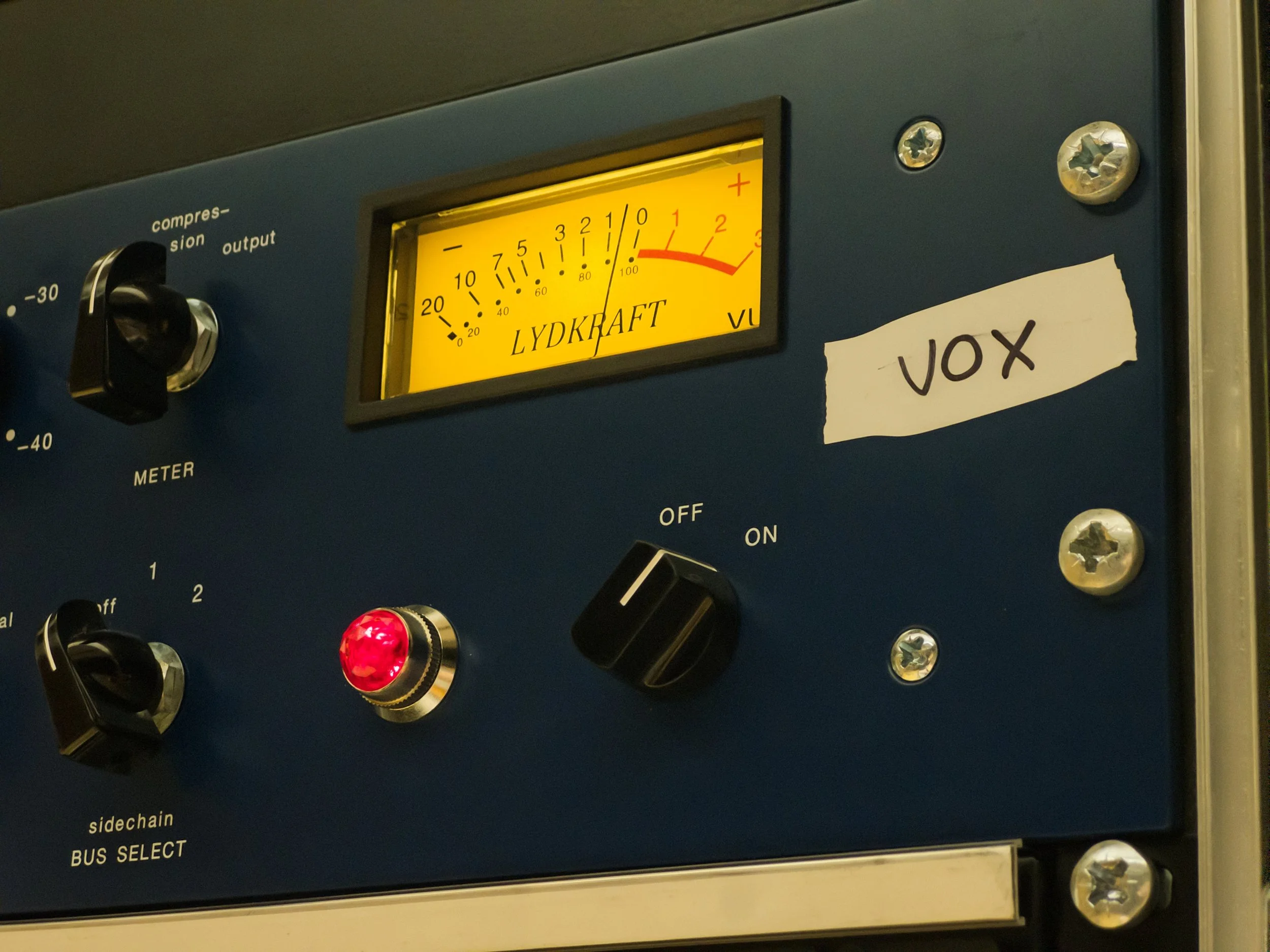 A blue audio compressor with the label 'VOX' in use in a recording studio.