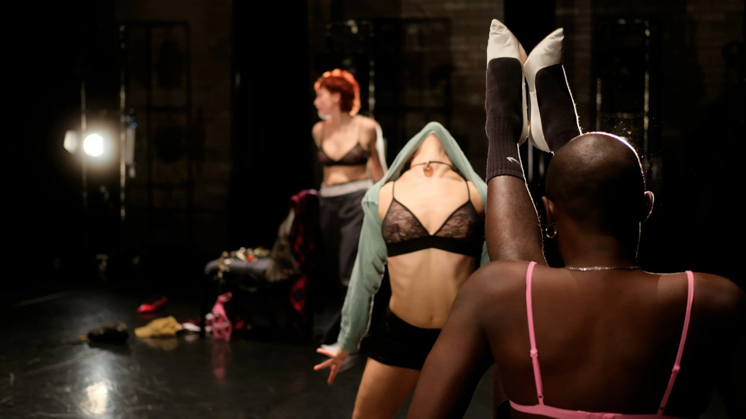 Image shows three queer performers on stage in various states of undress, all of them being expressively dramatic.