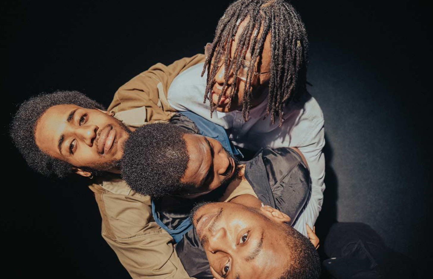 Image shows 4 black male performers looking up into the camera, they are embracing. Movement Direction by Alicia Meehan