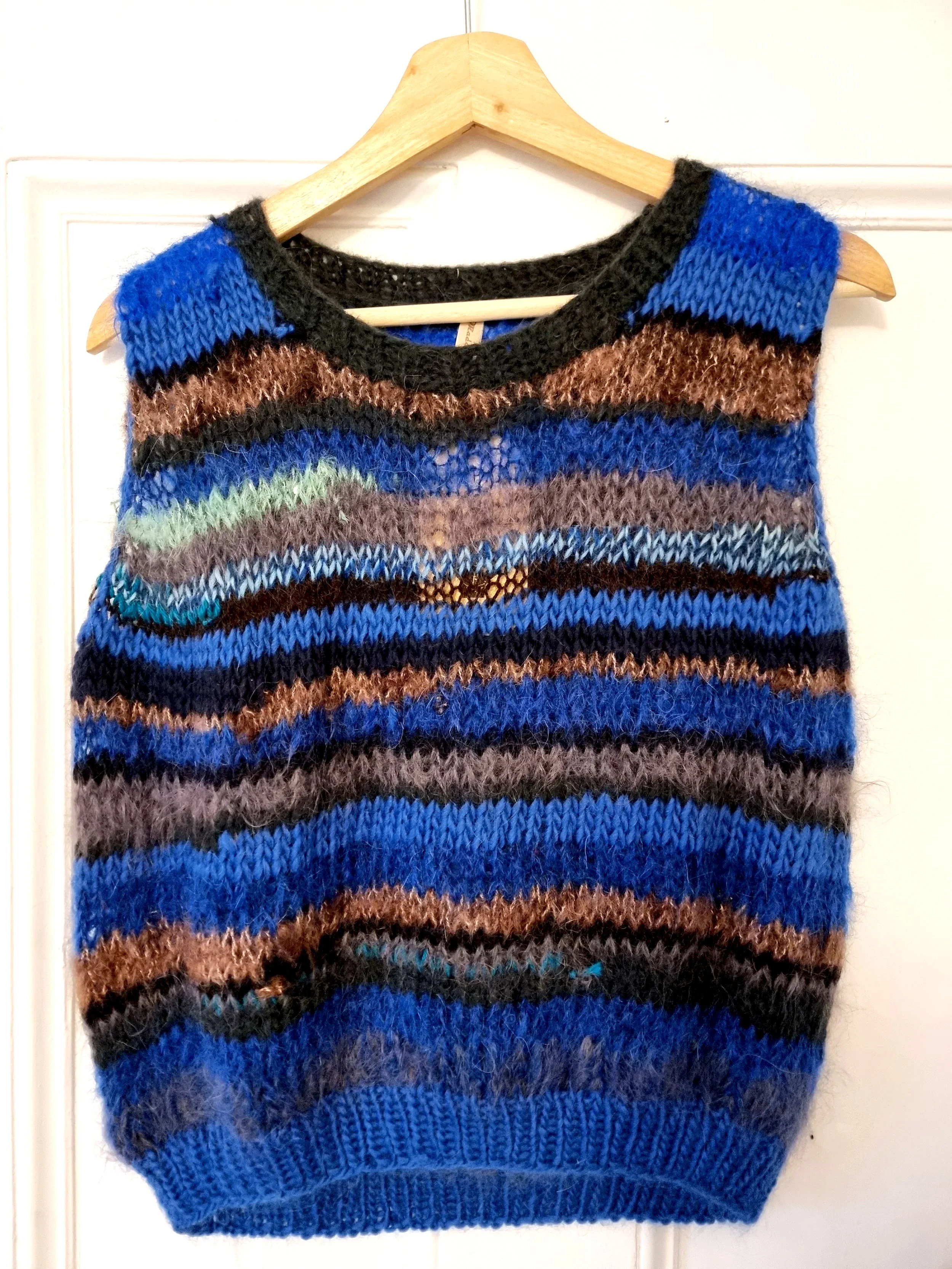 Colorful knitted sleeveless sweater hanging on a wooden hanger.