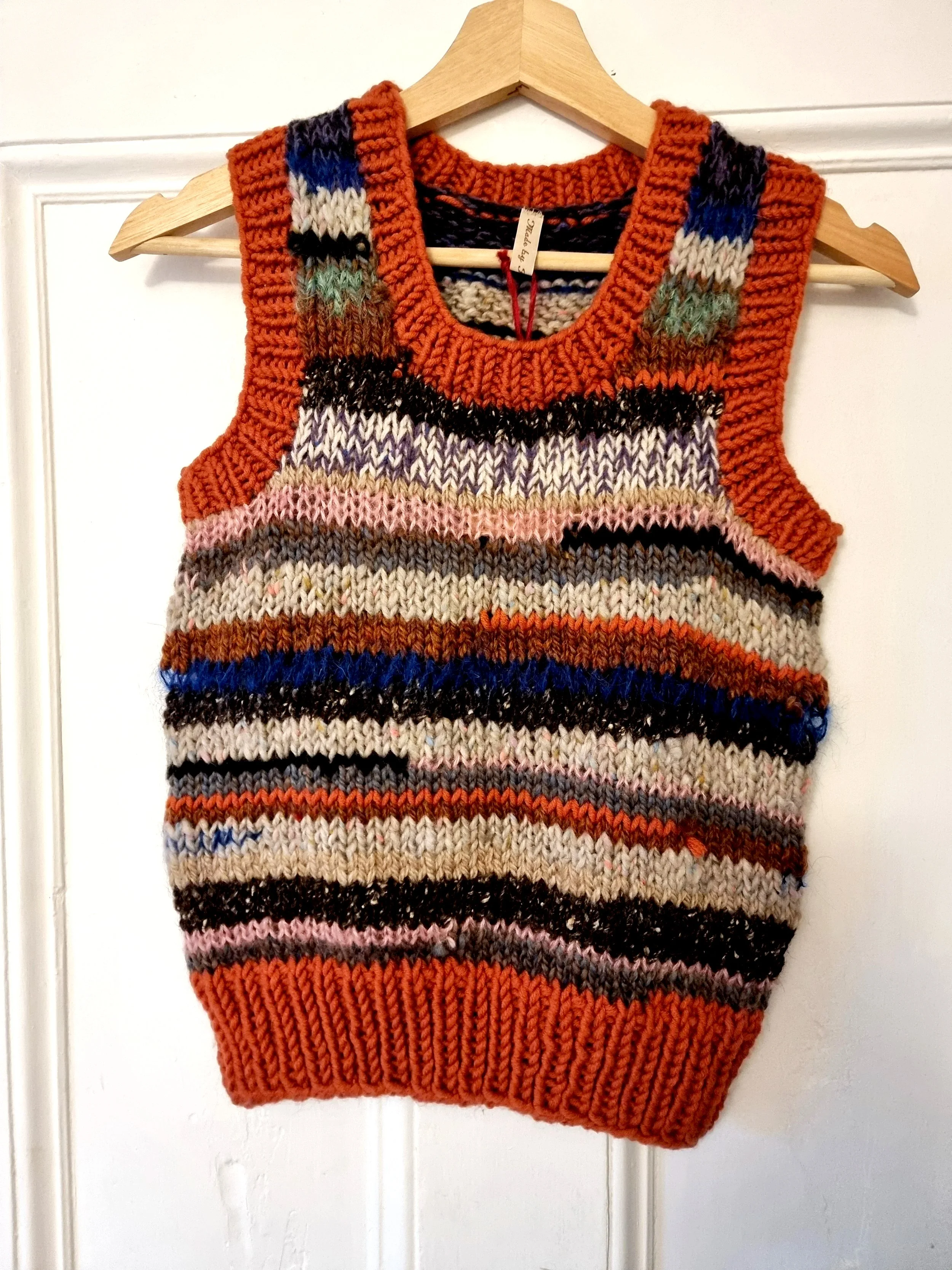 Colorful, striped knitted sweater vest hanging on a wooden hanger.