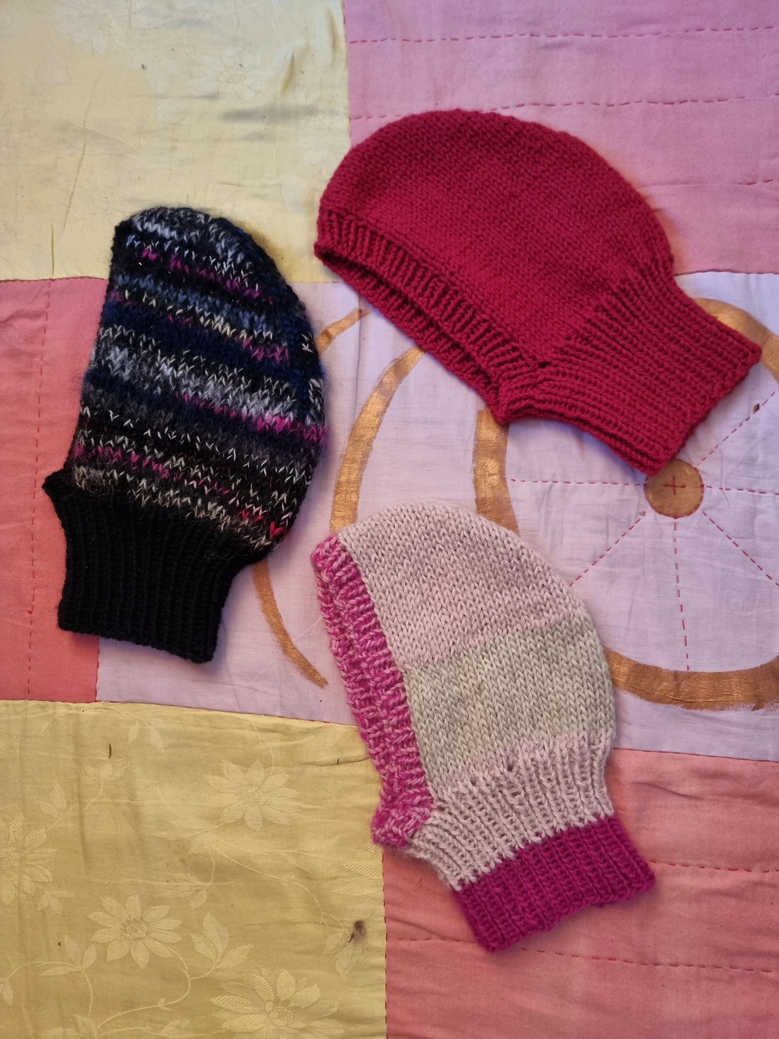 Three knit balaclavas placed on a patchwork fabric surface.