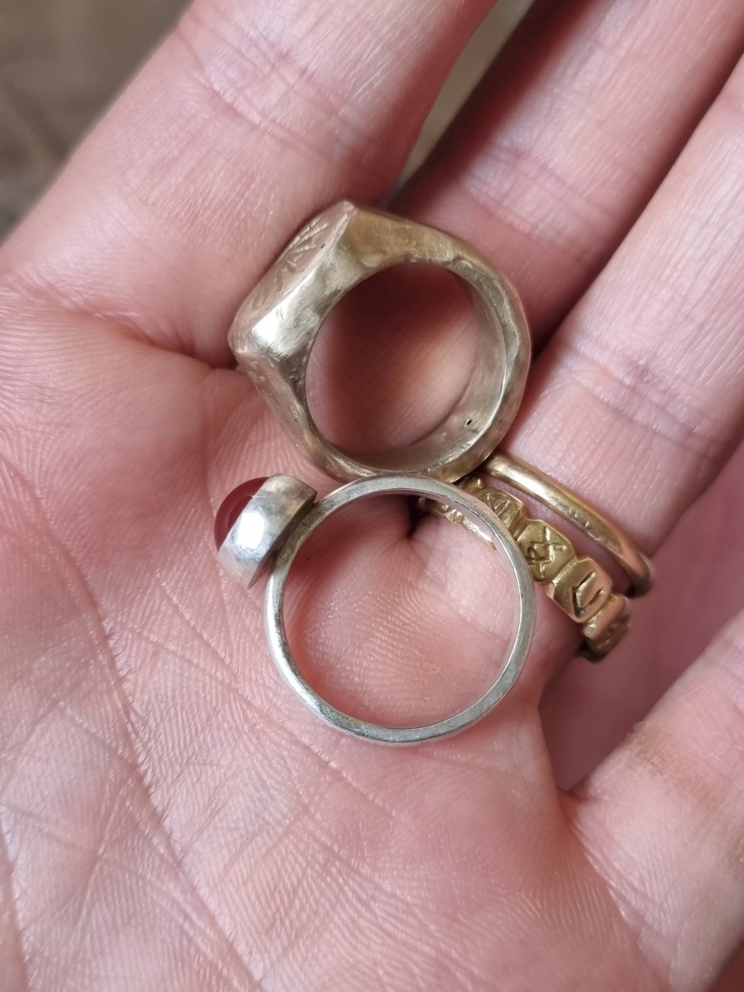 Close-up of two rings, two silver and one gold, held on person's fingers.