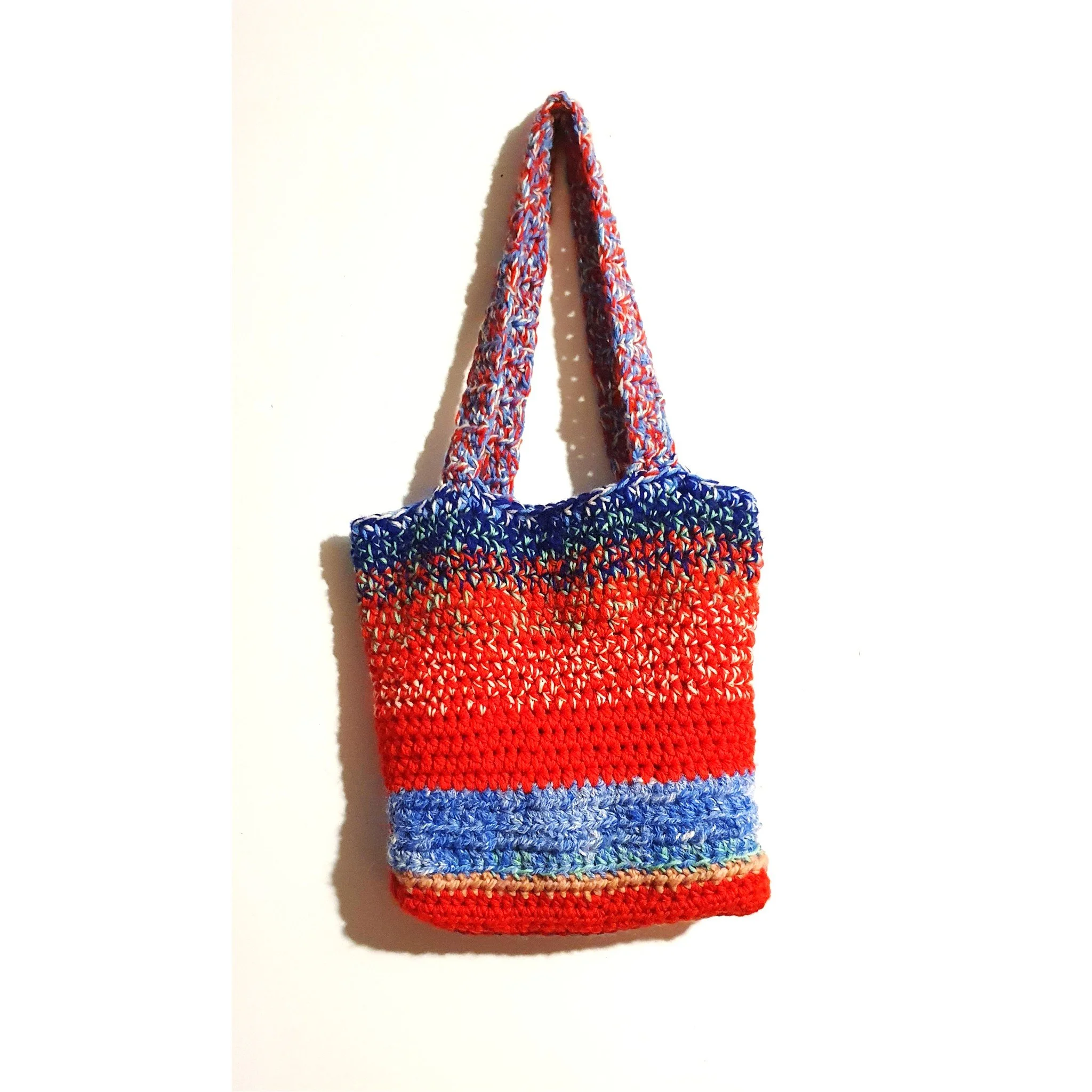 Colorful crocheted tote bag hanging on a white wall.