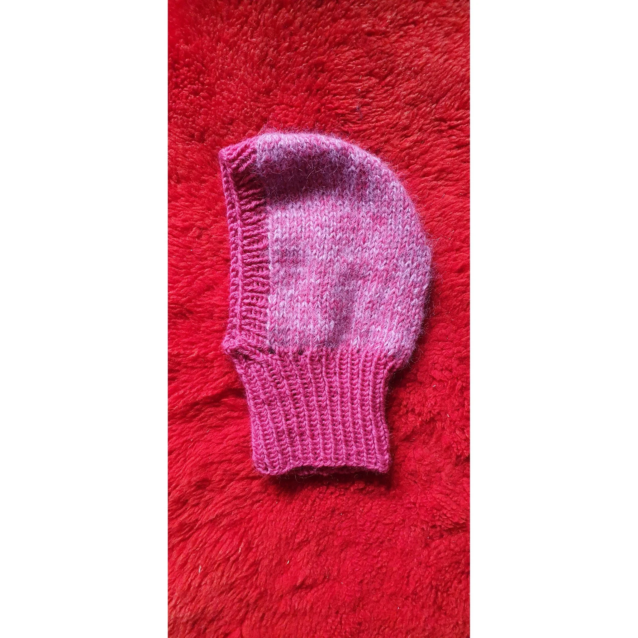 Pink knitted balaclava on red fuzzy background.