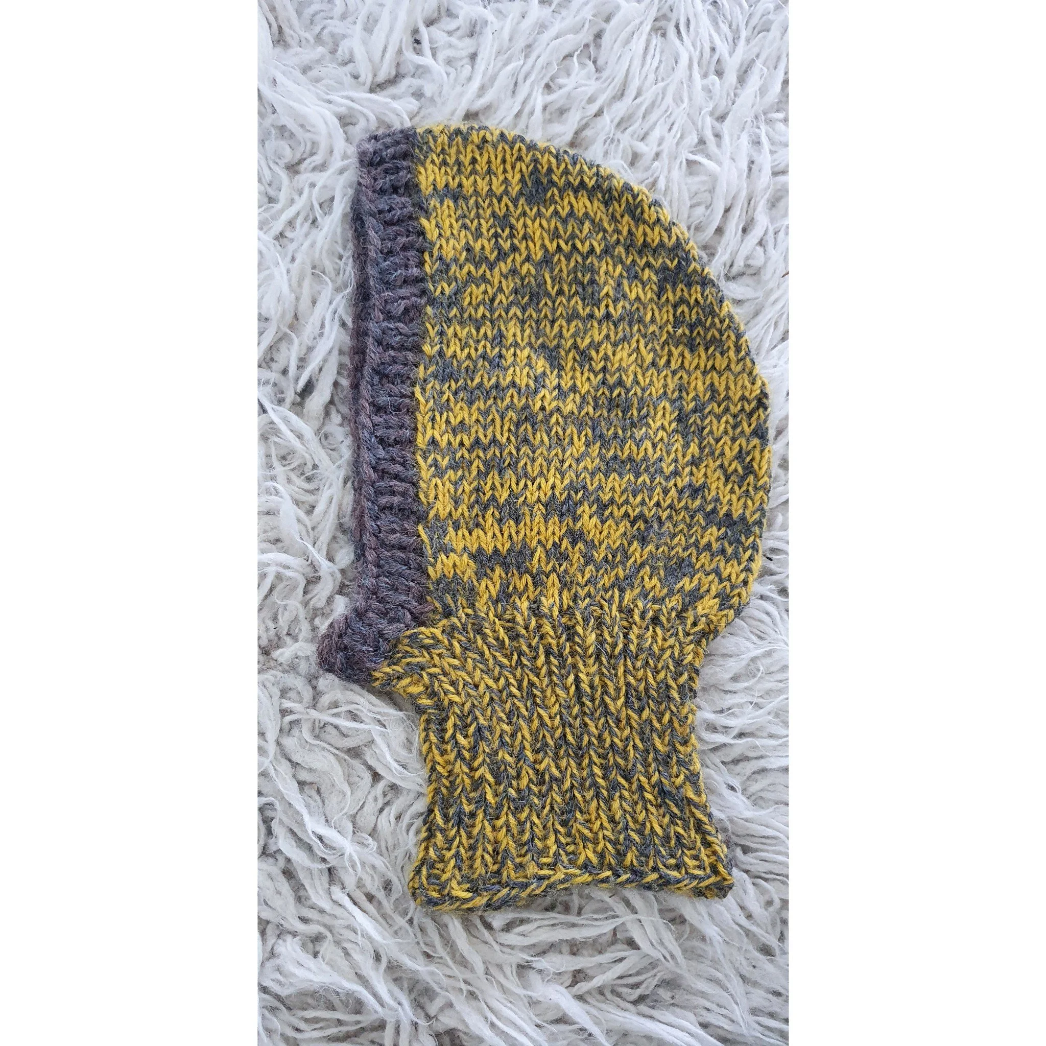 A knitted yellow and gray balaclava placed on a white shaggy surface.