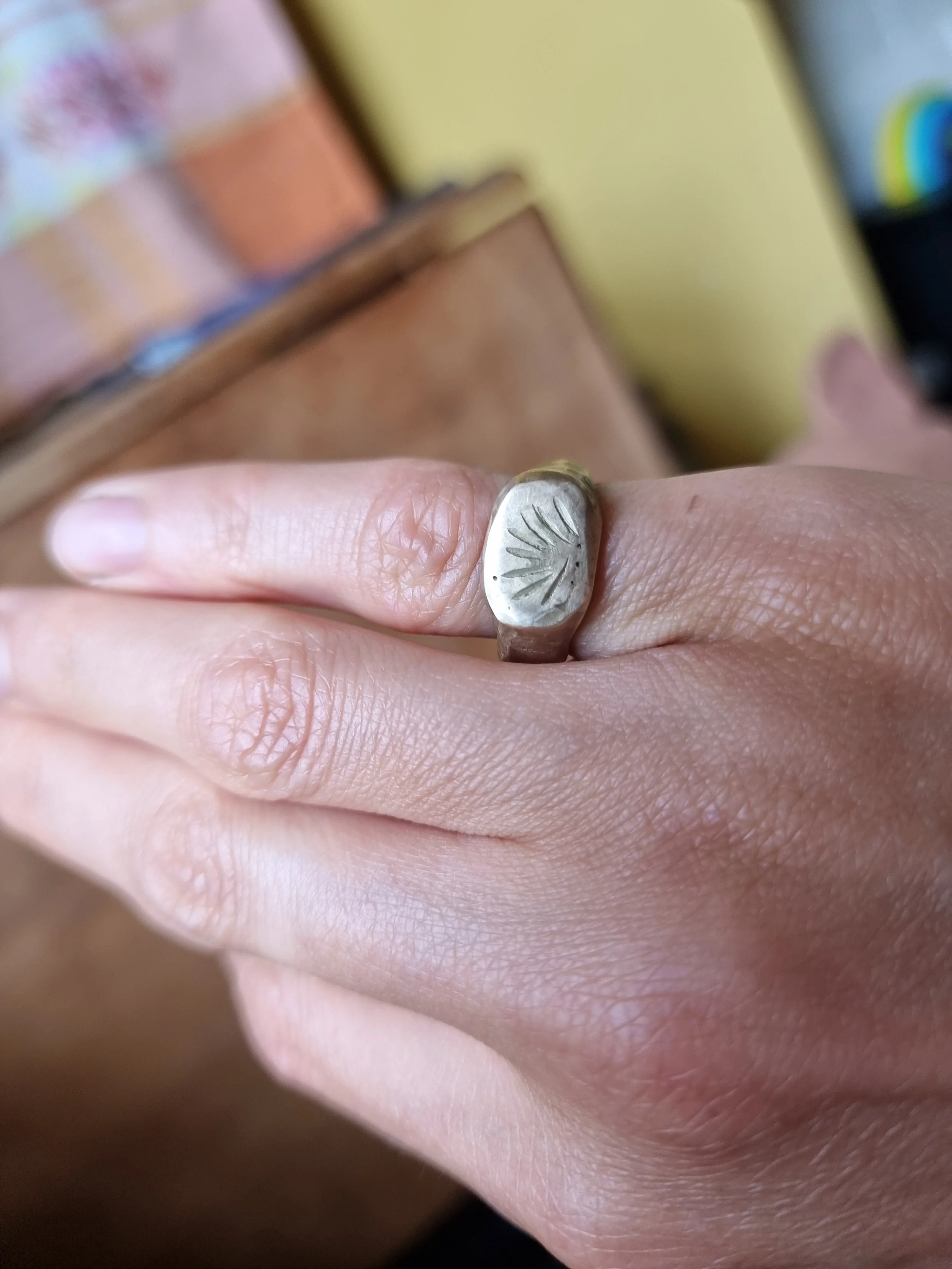 Close-up of a hand wearing a bronze ring with an engraved sunburst design.