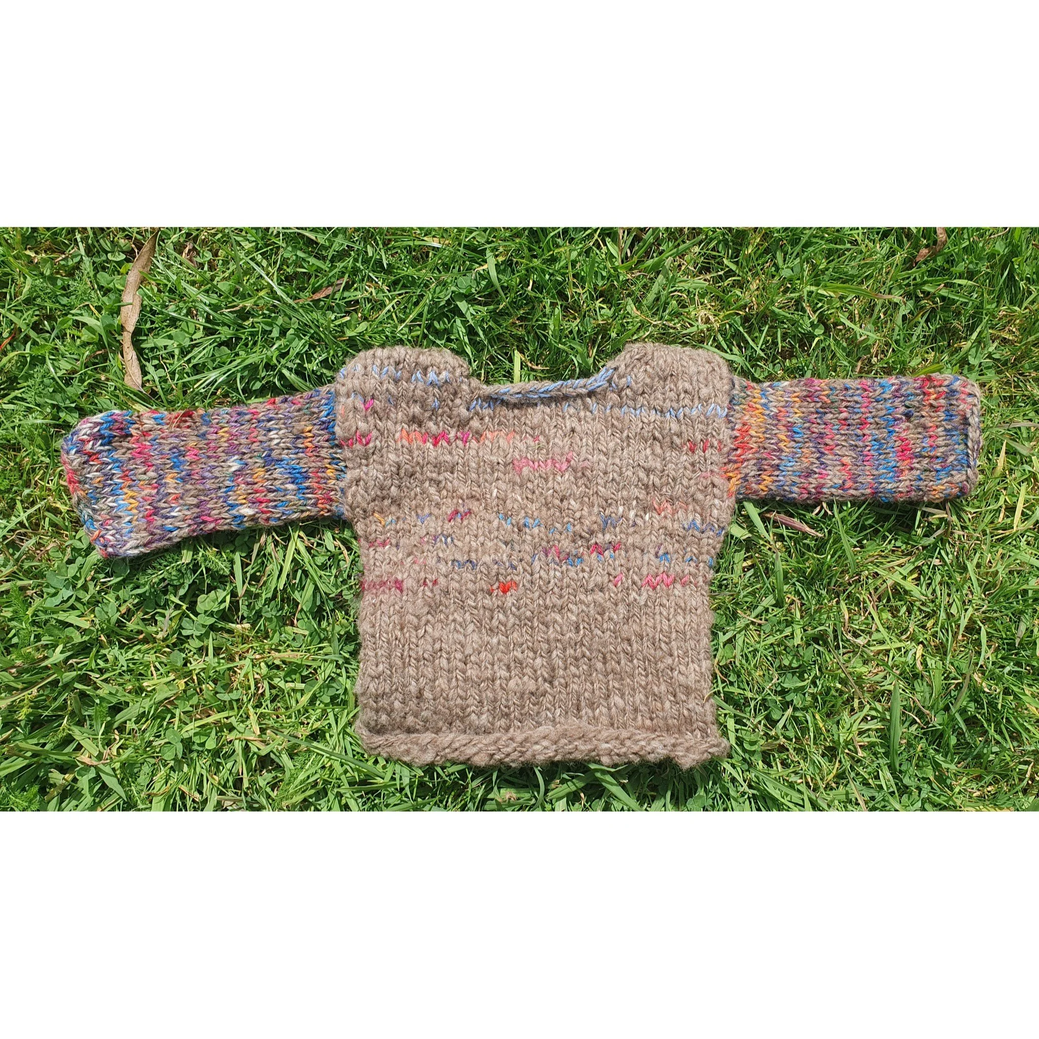 Knitted child sweater with multicolored sleeves lying on green grass