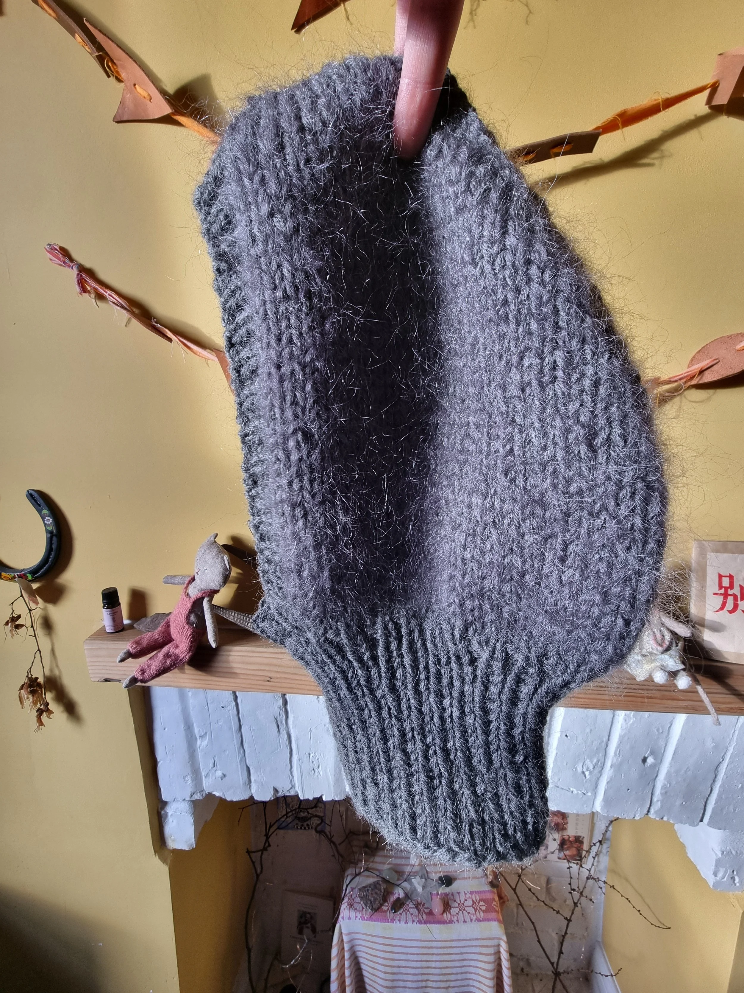 Gray knit balaclava hanging on a wooden peg against a yellow wall.