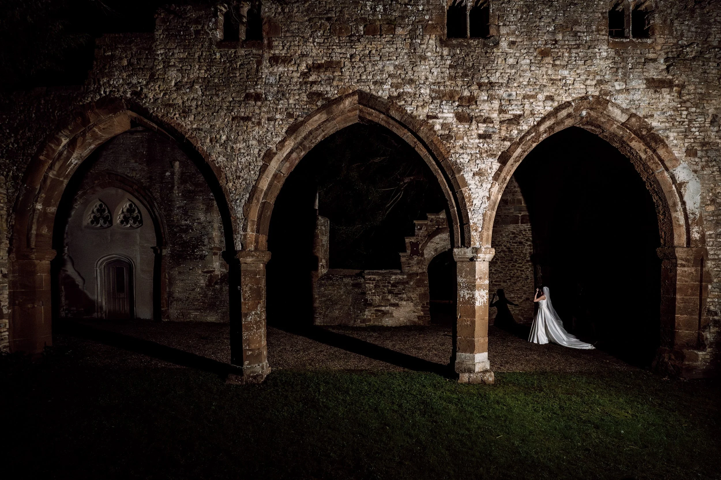 Nightitme portrait of a bride and groom walking through the old chapel at Ettington Park