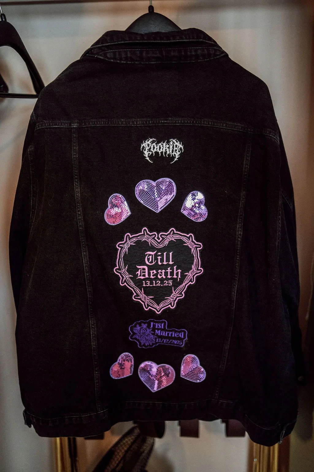 Back of a black denim jacket with pink and purple sequined heart patches, a barbed wire heart design with text 'Till Death 13.12.25', and a smaller patch that reads 'Just Married 13.12.2025'.