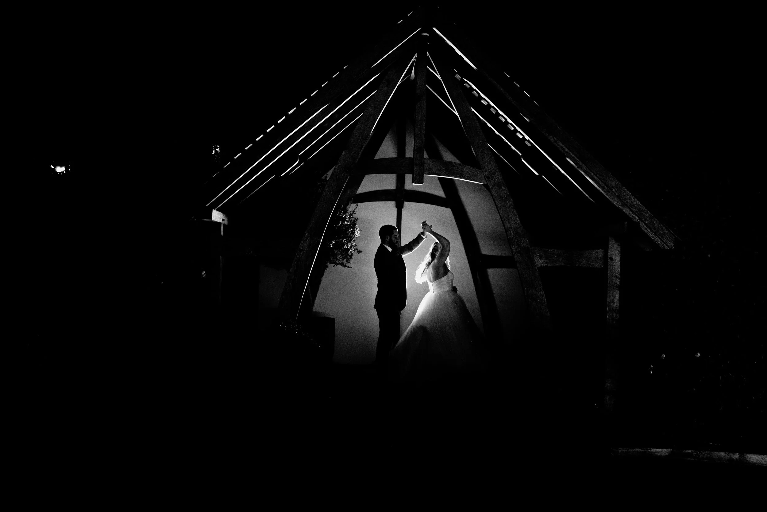 Silhouetted couple dancing under a wooden structure at night, with dramatic lighting highlighting their figures.