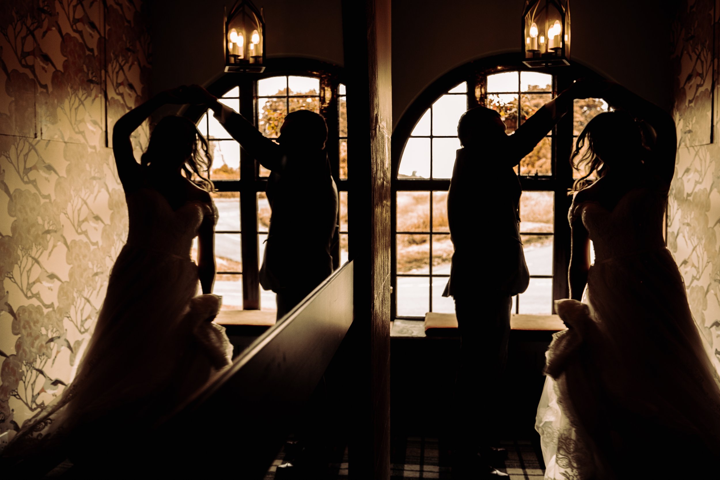 Silhouettes of a couple dancing inside near a window with floral wallpaper and hanging lamps, backlit by warm sunlight.