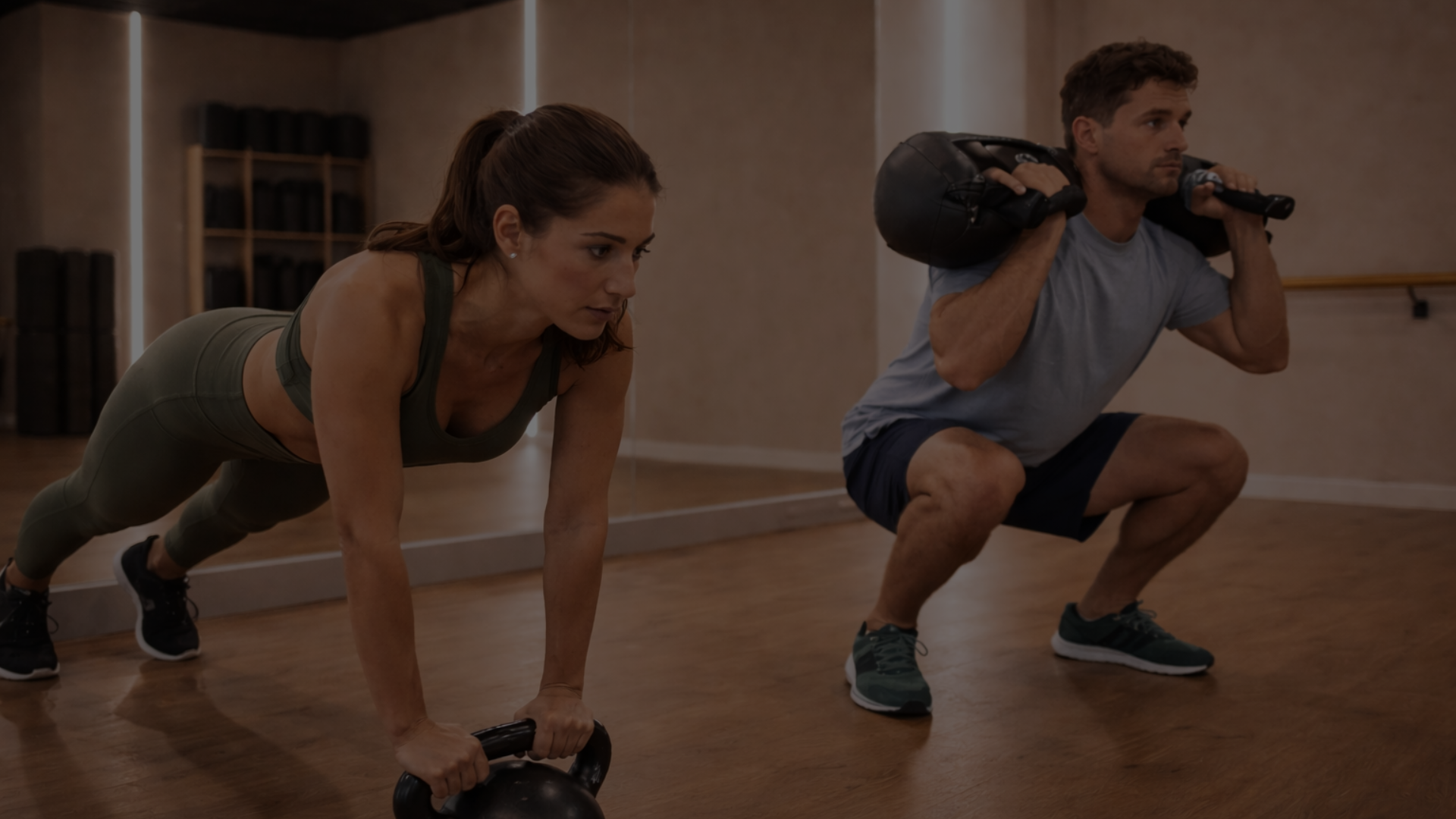 Hombre y mujer haciendo ejercicio en un gimnasio, con pesas y piso de madera.