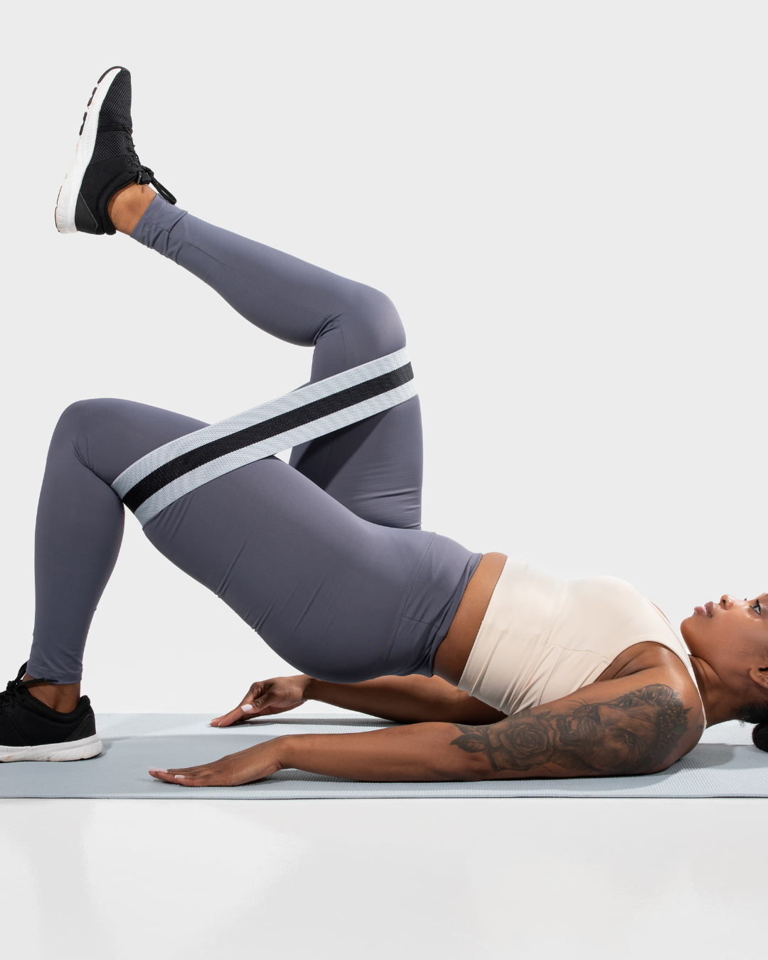 Mujer haciendo ejercicio con banda de resistencia en piernas, acostada en colchoneta, en posición de puente.