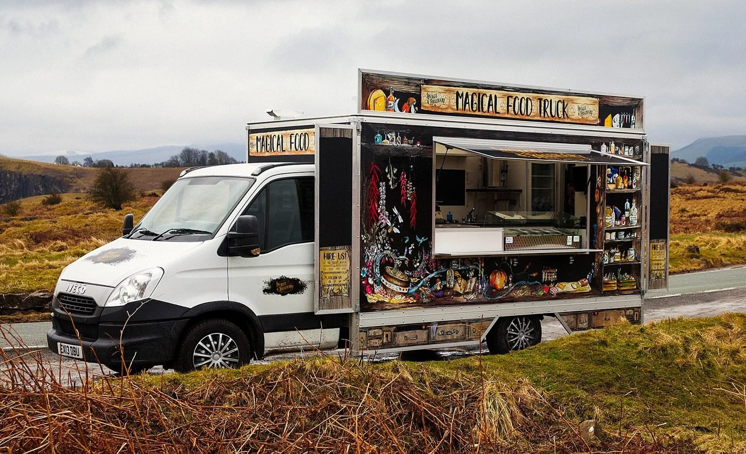 A food truck labeled 'Lovage and Rosemary' parked on the side of a rural road, with a painted exterior featuring colorful artwork and signs, in a landscape of rolling hills and cloudy sky.