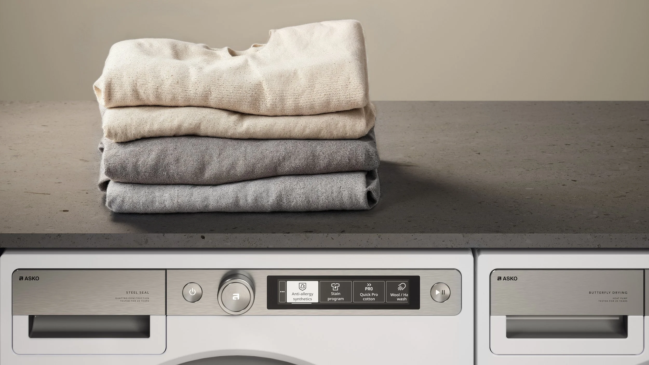 Stacked beige, gray, and light gray folded clothes on a washing machine with digital controls.