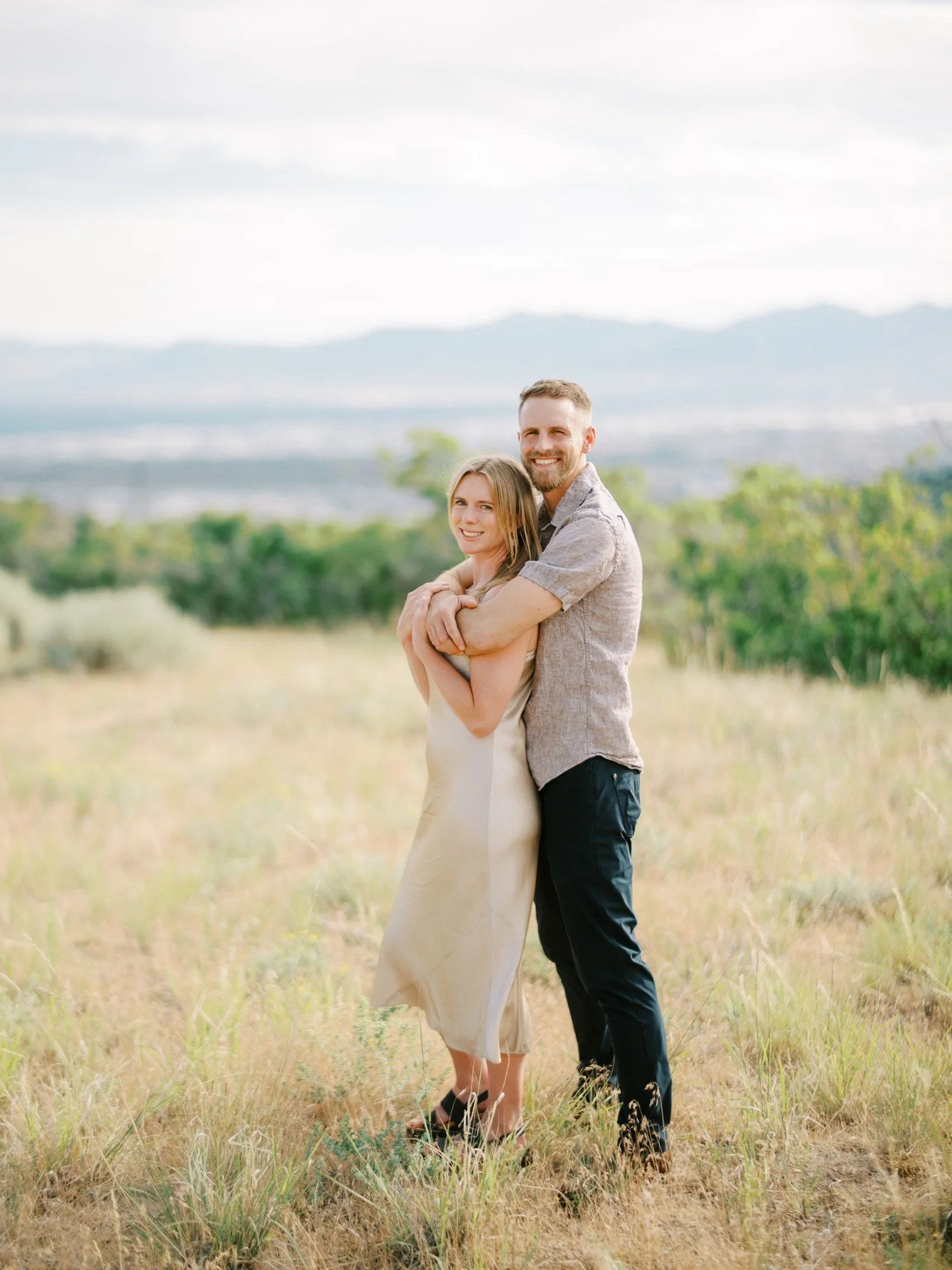Engaged couple embracing in a grassy Northern Utah field